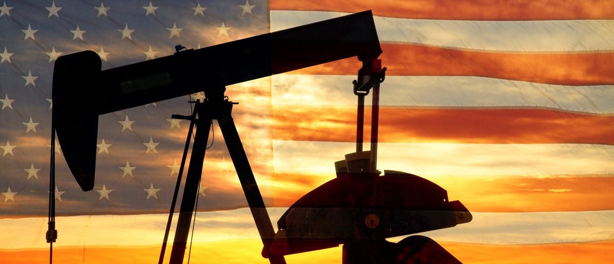 Landscape image of a oil well pumpjack wiith an early morning golden sunrise and American USA red White and Blue Flag background. (Shutterstock/James BO Insogna)