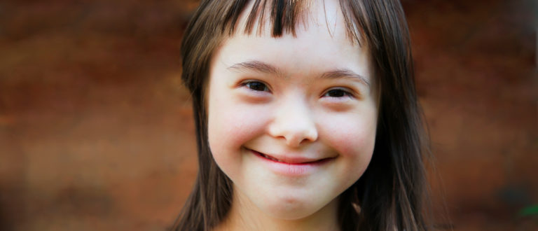 Cute-smiling-down-syndrome-girl-on-the-brown-background-e1520460838410-768x330.jpg