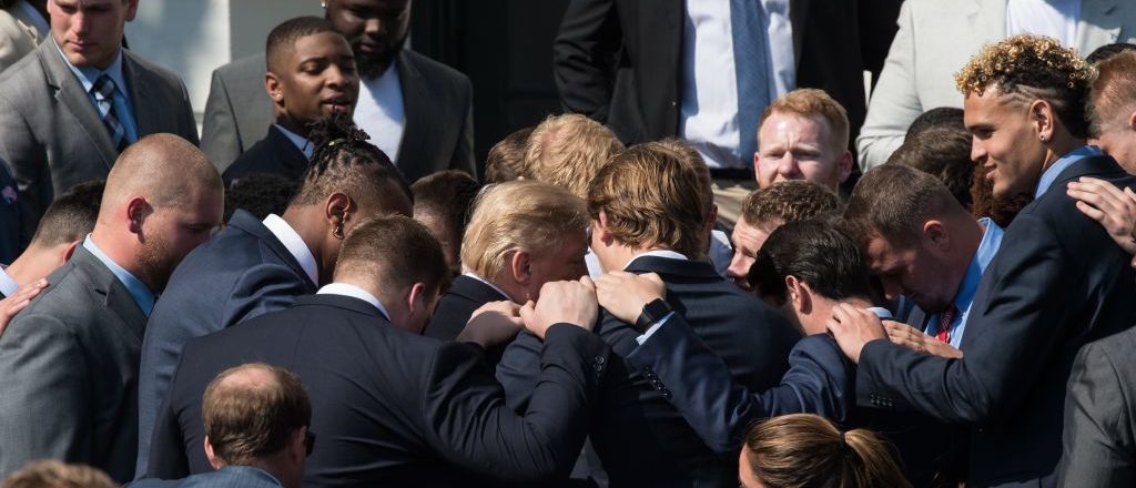 US President Donald Trump prays with members of the 2017 NCAA football national champions the Alabama Crimson Tide at the White House in Washington, DC, on April 10, 2018. / AFP PHOTO / NICHOLAS KAMM        (Photo credit: NICHOLAS KAMM/AFP/Getty Images)