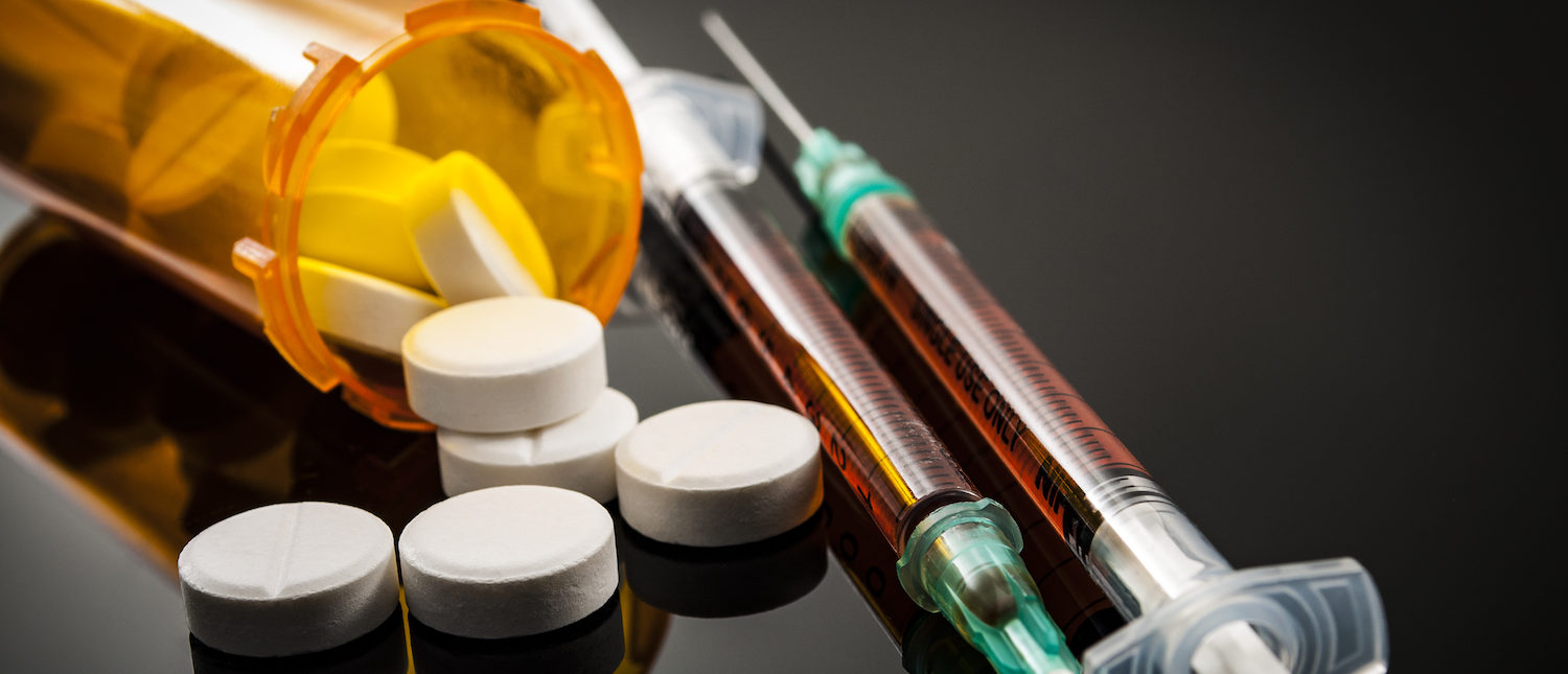 Opioid epidemic, drug abuse concept with closeup on two heroin syringes or other narcotics surrounded by scattered prescription opioids. Oxycodone is the generic name for a range of opioid painkillers. (Shutterstock/Victor Moussa) | New DEA Rule Combats Black Market Opioids