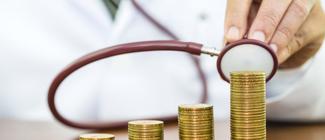 Doctor hand holding stethoscope checking stack of money coins arranged as a graph on wooden table, concept of financial health check and medical expenses