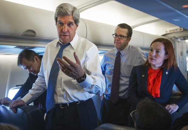 Jen Psaki stands behind Secretary of State John Kerry as he talks with reporters aboard his government aircraft shortly after departing Seoul Air Base April 13, 2013, for Beijing, China