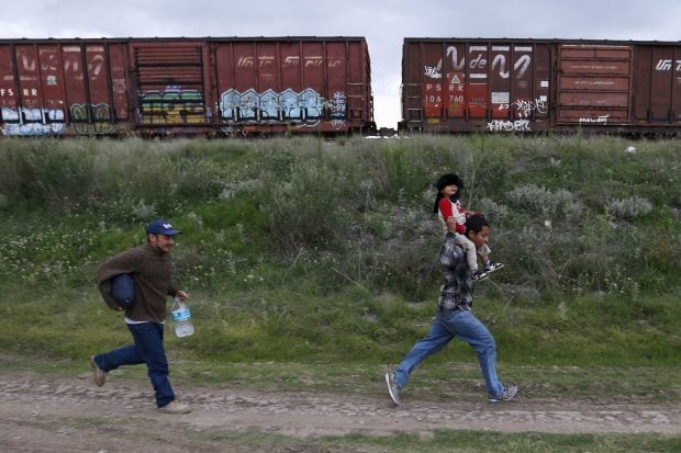 A Salvadoran father (R) carries his son while running next to another immigrant as they try to board a train heading to the Mexican-U.S. border, in Huehuetoca, near of Mexico City, June 1, 2015. An increasing number of Central Americans are sneaking across Mexico's border en route to the United States. Picture taken June 1, 2015. REUTERS/Edgard Garrido - RTR4YKNV