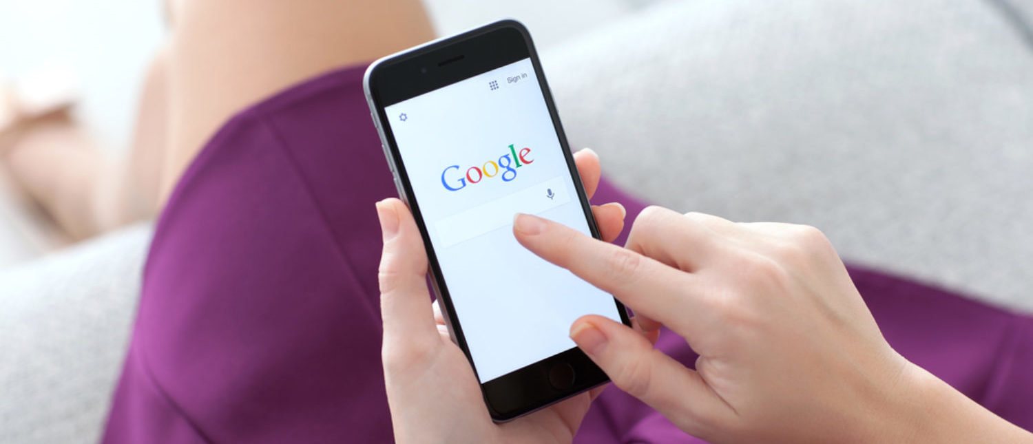 Woman holding a smartphone while searching through Google. [Shutterstock - Denys Prykhodov]