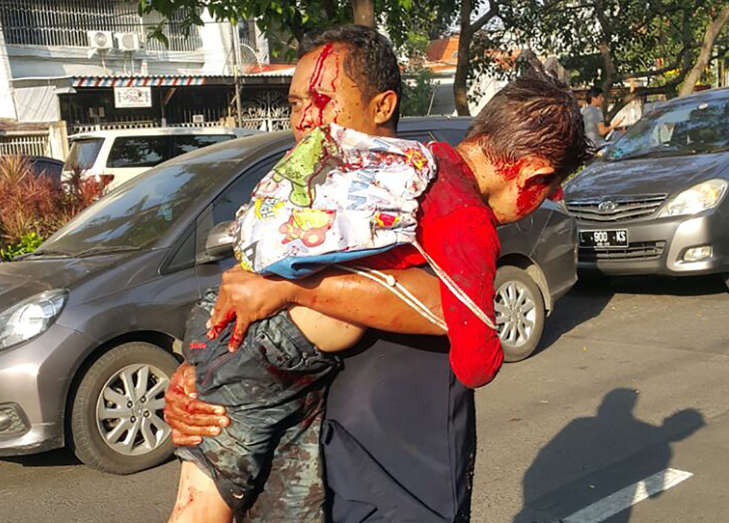 A man carries an injured child away from the scene of a suicide bombing at a church in Surabaya, Indonesia on May 13, 2018. PHOTO: TheDCNF