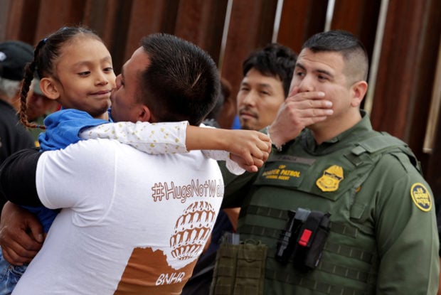 A man embraces a child as an U.S. border patrol federal agent reacts during a brief reunification meeting of relatives separated by deportation and immigration called "Hugs, No Walls", at the border fence between Mexico and U.S in Ciudad Juarez, Mexico October 13, 2018. REUTERS/Jose Luis Gonzalez
