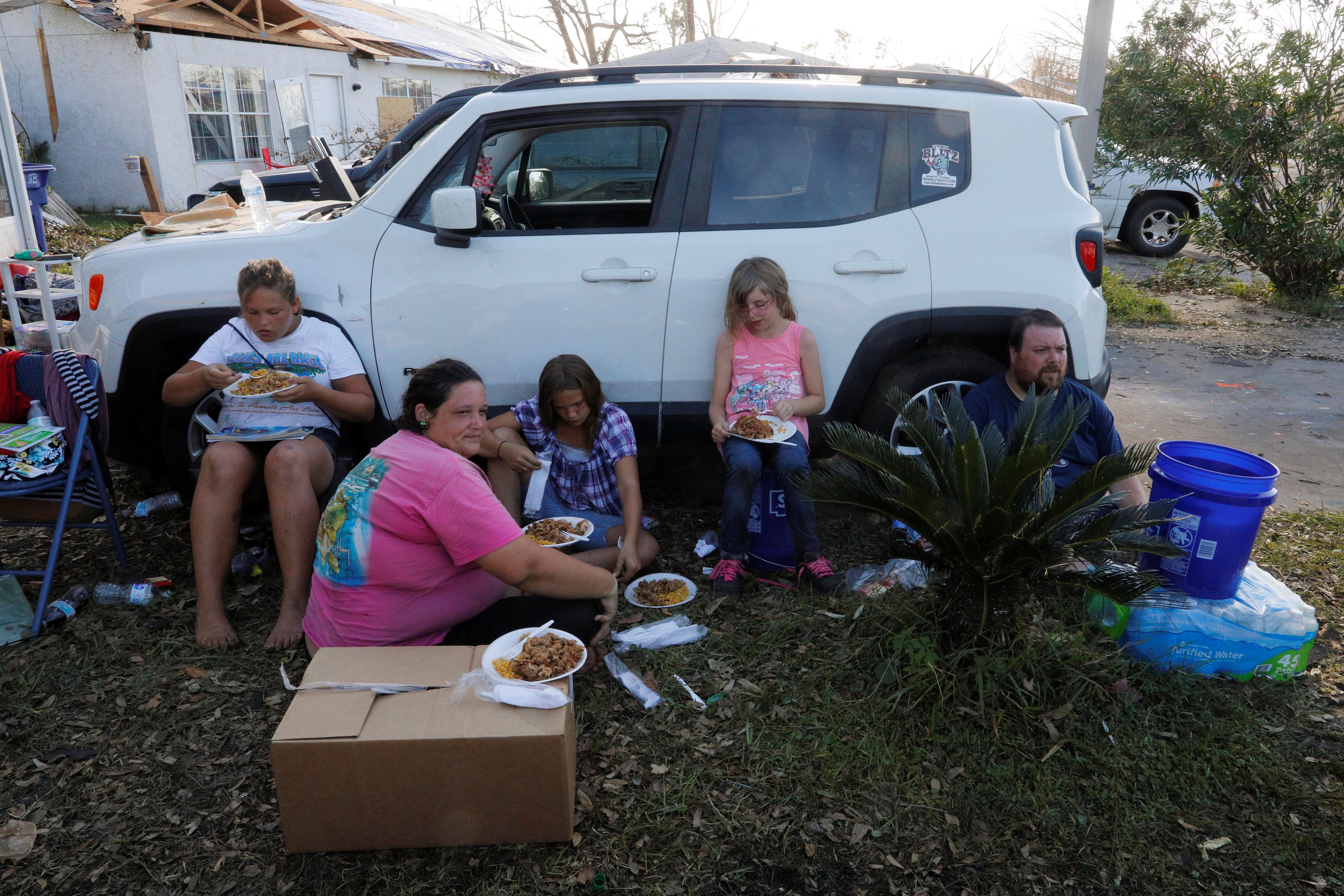 The Lachance family eats hot food outside their home damaged by Hurricane Michael in Panama City