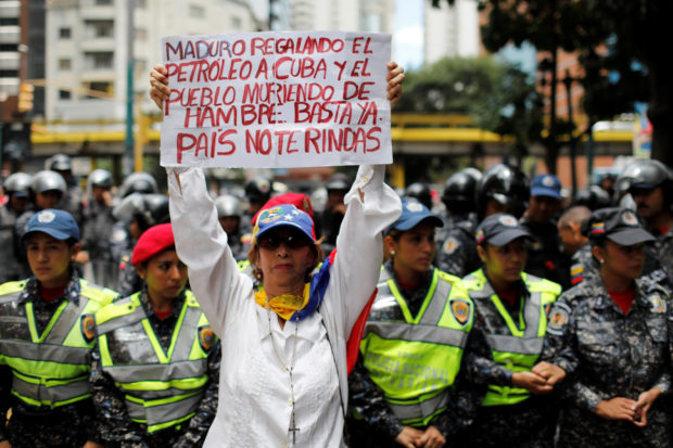 A woman holds a sign that reads: "Maduro gives oil to Cuba and people die of hunger. Enough. Country do not give up" during a protest of workers of the health sector due to the shortages of medicines and for higher wages, outside a public children hospital in Caracas, Venezuela August 16, 2018. REUTERS/Marco Bello