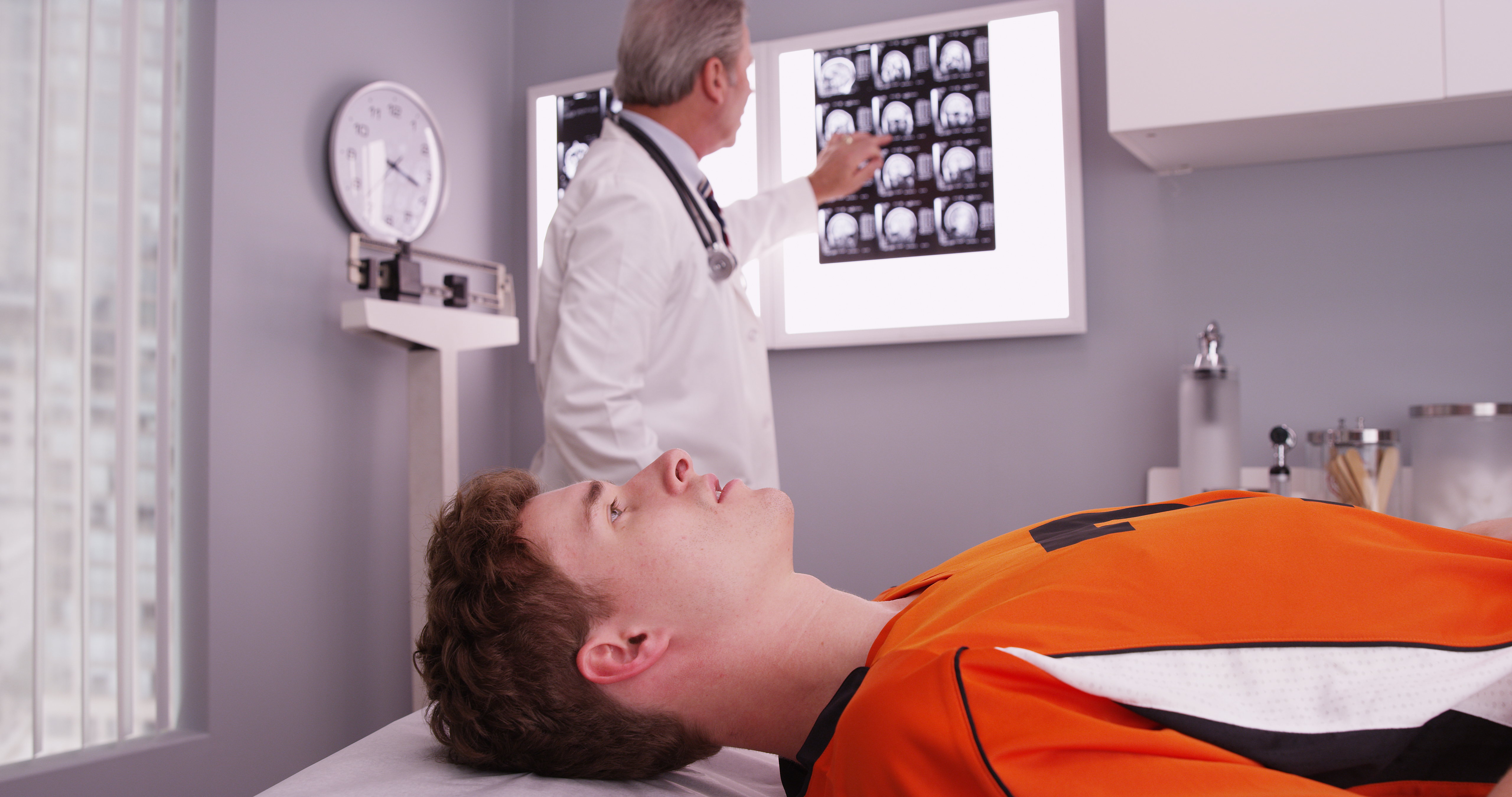 Pictured is a football player lyding down while a doctor reviews his x-rays. SHUTTERSTOCK/ Rocketclips, Inc. 