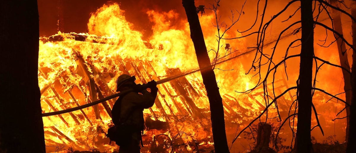 MAGALIA, CA - NOVEMBER 09: A Cal Fire firefighter sprays water on a home next to a burning home as the Camp Fire moves through the area on November 9, 2018 in Magalia, California. Fueled by high winds and low humidity, the rapidly spreading Camp Fire ripped through the town of Paradise and has quickly charred 70,000 acres and has destroyed numerous homes and businesses in a matter of hours. The fire is currently at five percent containment. (Photo by Justin Sullivan/Getty Images)