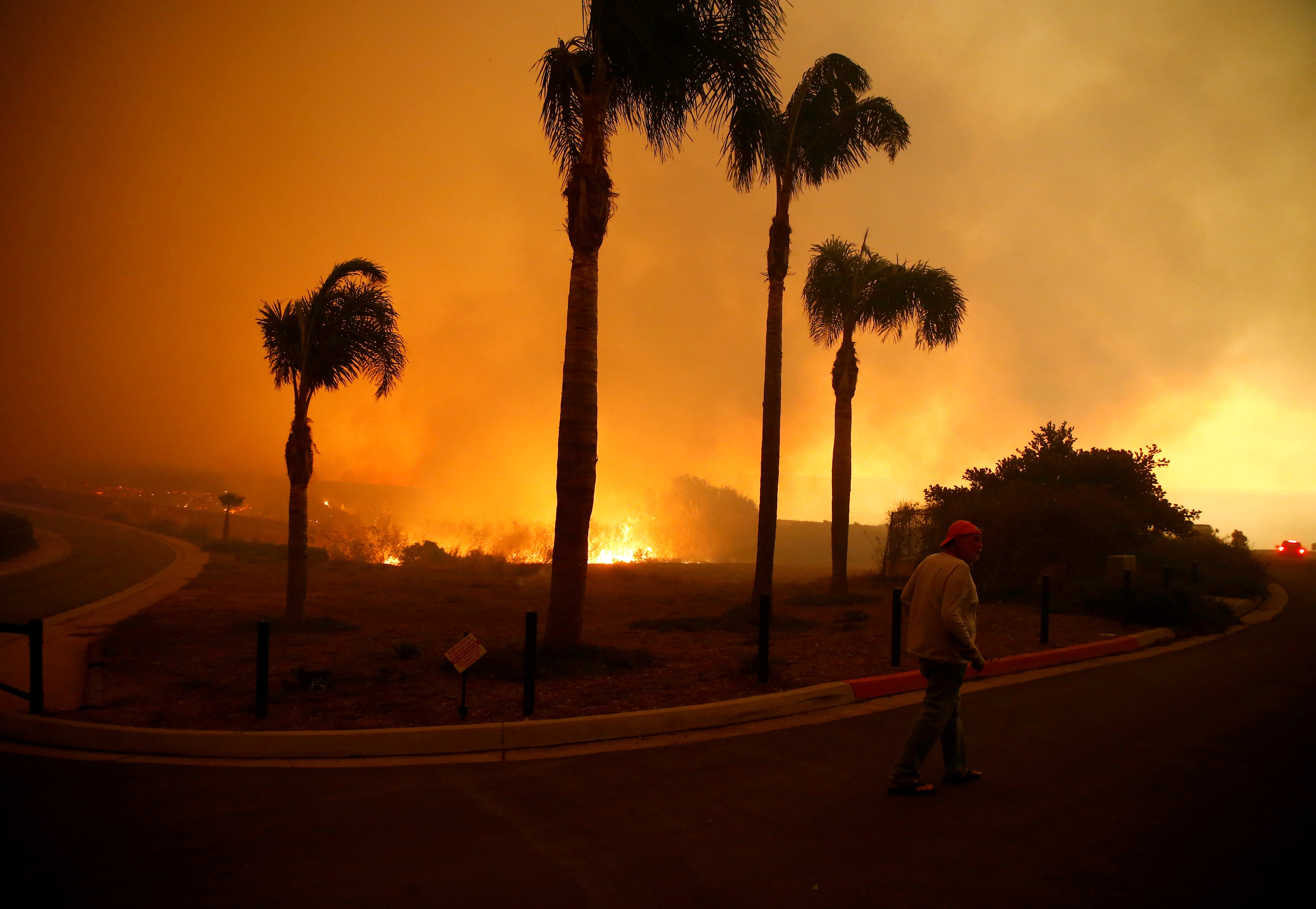 A man walks through a neighborhood threatened by flames as the Woolsey Fire burns in Malibu