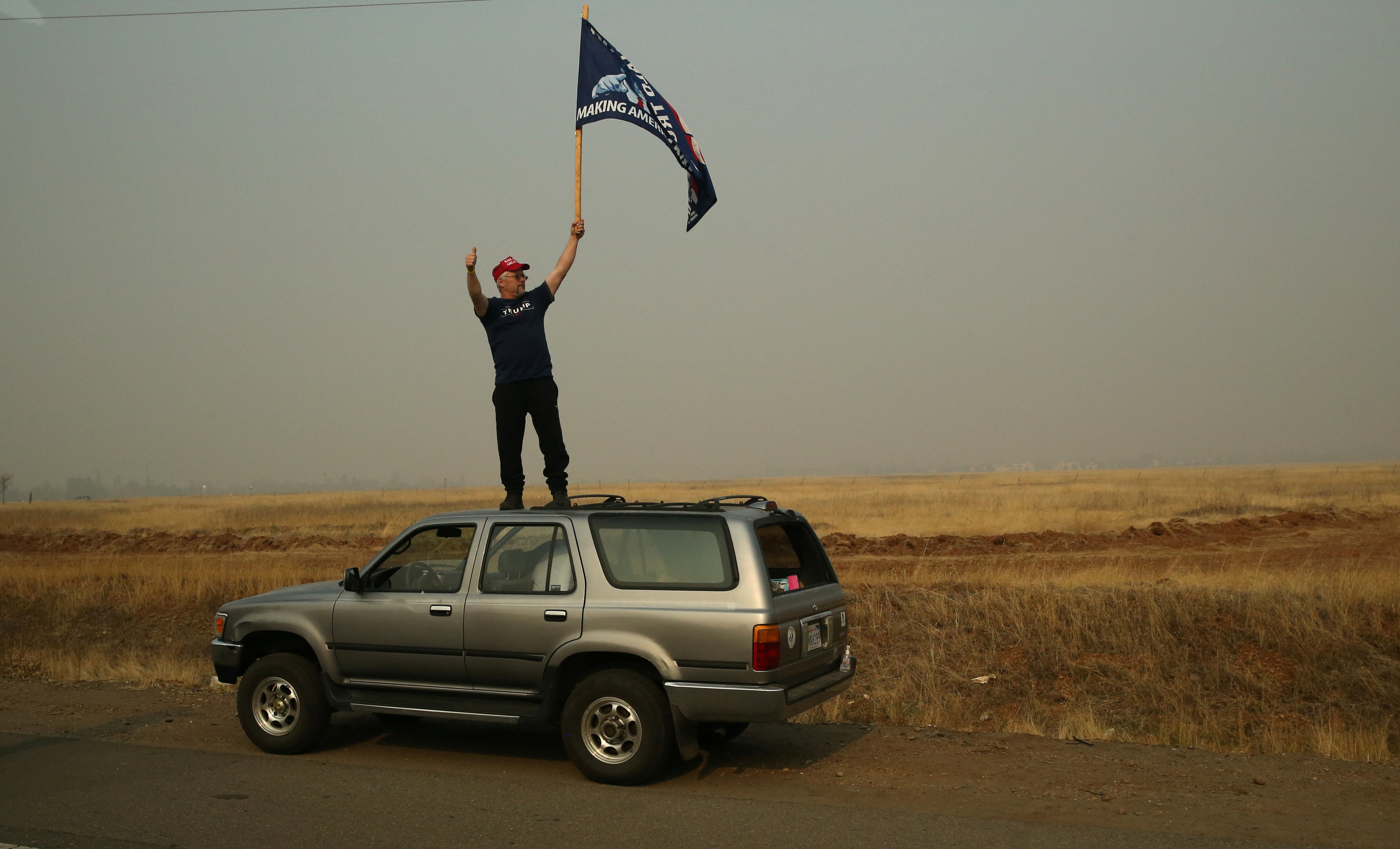 A man waves a Trump flag as the motorcade of U.S. President Donald Trump flies by after Trump visited a neighborhood recently destroyed by the Camp fire in Paradise, California, U.S.