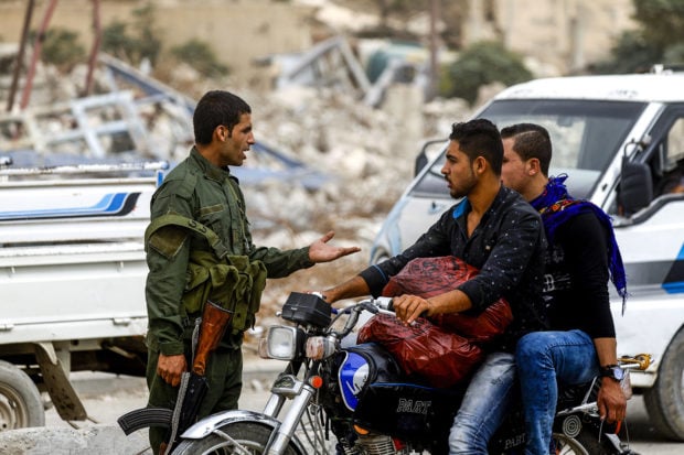 A member of the Raqa civil council's local security forces speaks with a rider on a motorcycle at a checkpoint securing vehicles entering into the eastern Syrian city and former Islamic State (IS) group stronghold, on October 16, 2018. - A year after Kurdish and allied forces drove the Islamic State group from the northern Syrian city of Raqa, traumatised civilians still live in fear of near-daily bombings. DELIL SOULEIMAN/AFP/Getty Images