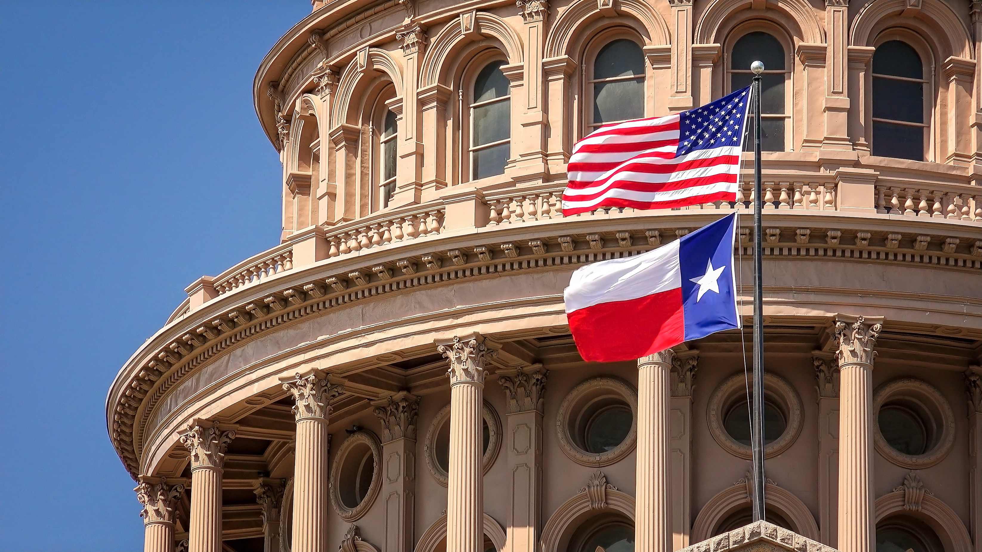 American and Texas state flags flying on the dome of the Texas State Capitol building in Austin [Shutterstock]