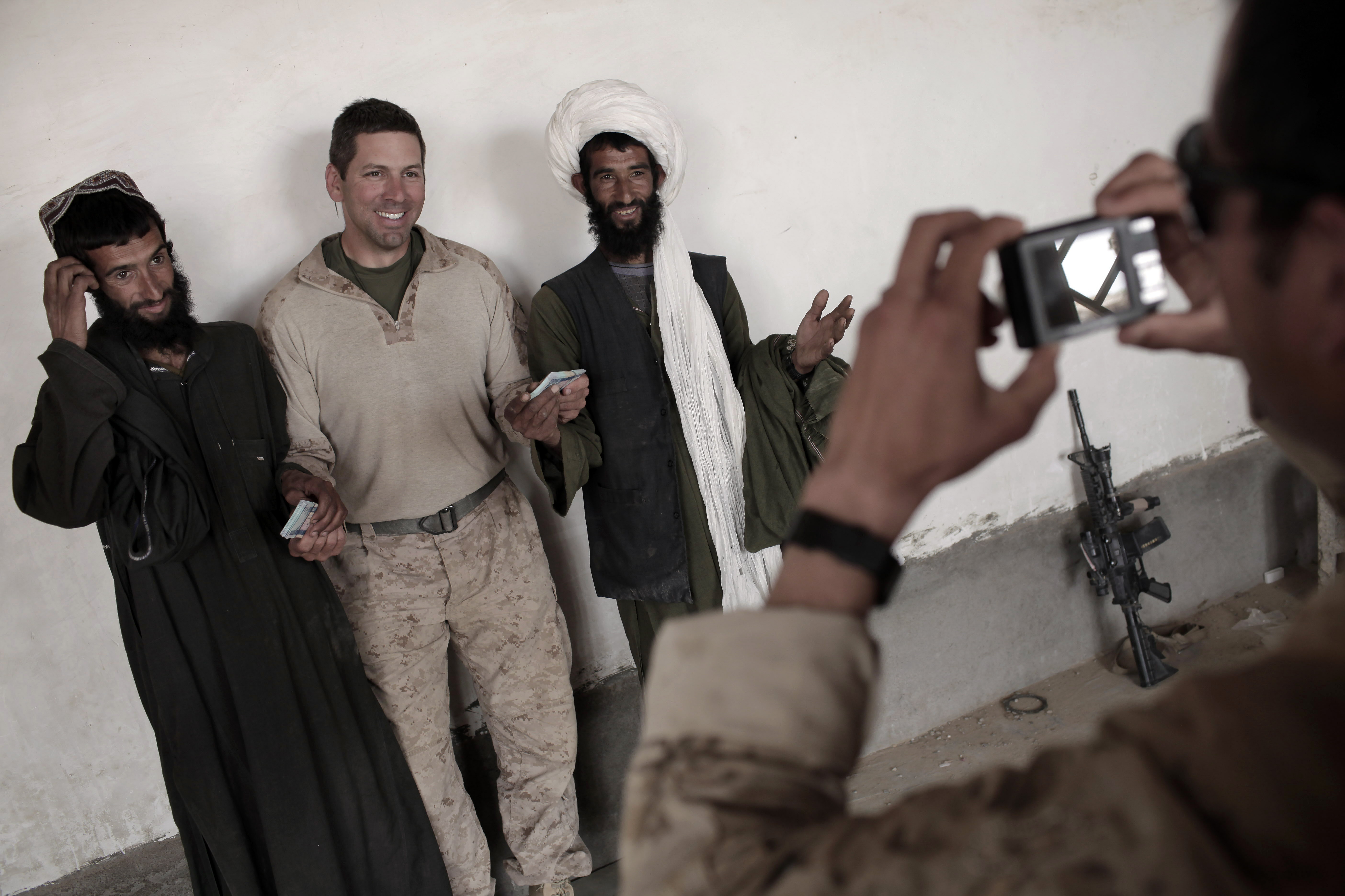 An interpreter for U.S. Marines of India Company, 3rd Battalion, 6th Marines takes a souvenir picture requested by the US officer giving 20,000 Afghanis each to two brothers for damages to their residences caused during the ongoing US military offensive against Taliban insurgency, in Marjah, Helmand province, southern Afghanistan, on April 12, 2010. (MAURICIO LIMA/AFP/Getty Images)