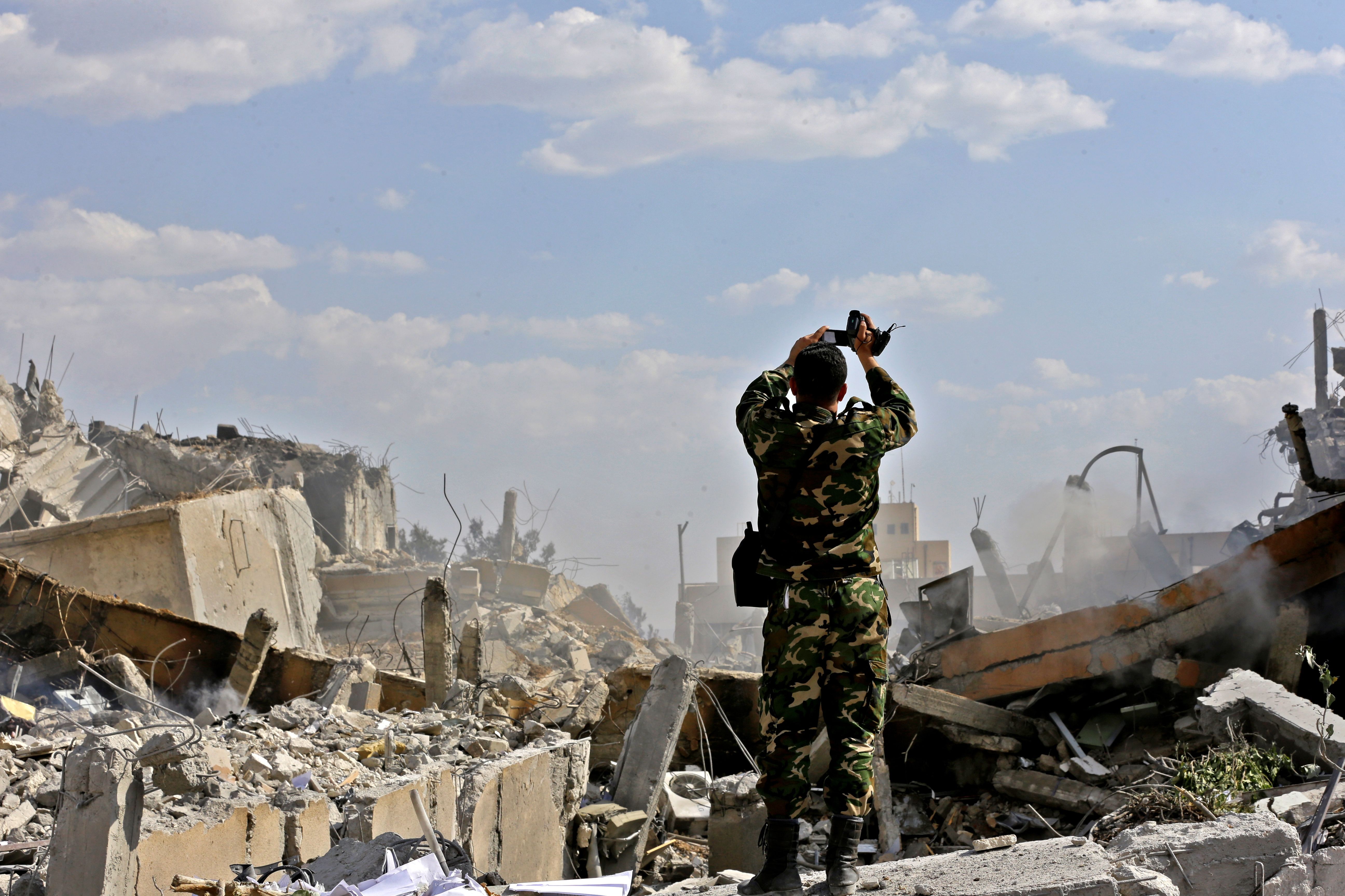 TOPSHOT - A Syrian soldier inspects the wreckage of a building described as part of the Scientific Studies and Research Centre (SSRC) compound in the Barzeh district, north of Damascus, during a press tour organised by the Syrian information ministry, on April 14, 2018. - The United States, Britain and France launched strikes against Syrian President Bashar al-Assad's regime early on April 14 in response to an alleged chemical weapons attack after mulling military action for nearly a week. Syrian state news agency SANA reported several missiles hit a research centre in Barzeh, north of Damascus, "destroying a building that included scientific labs and a training centre". (Photo by LOUAI BESHARA / AFP) 