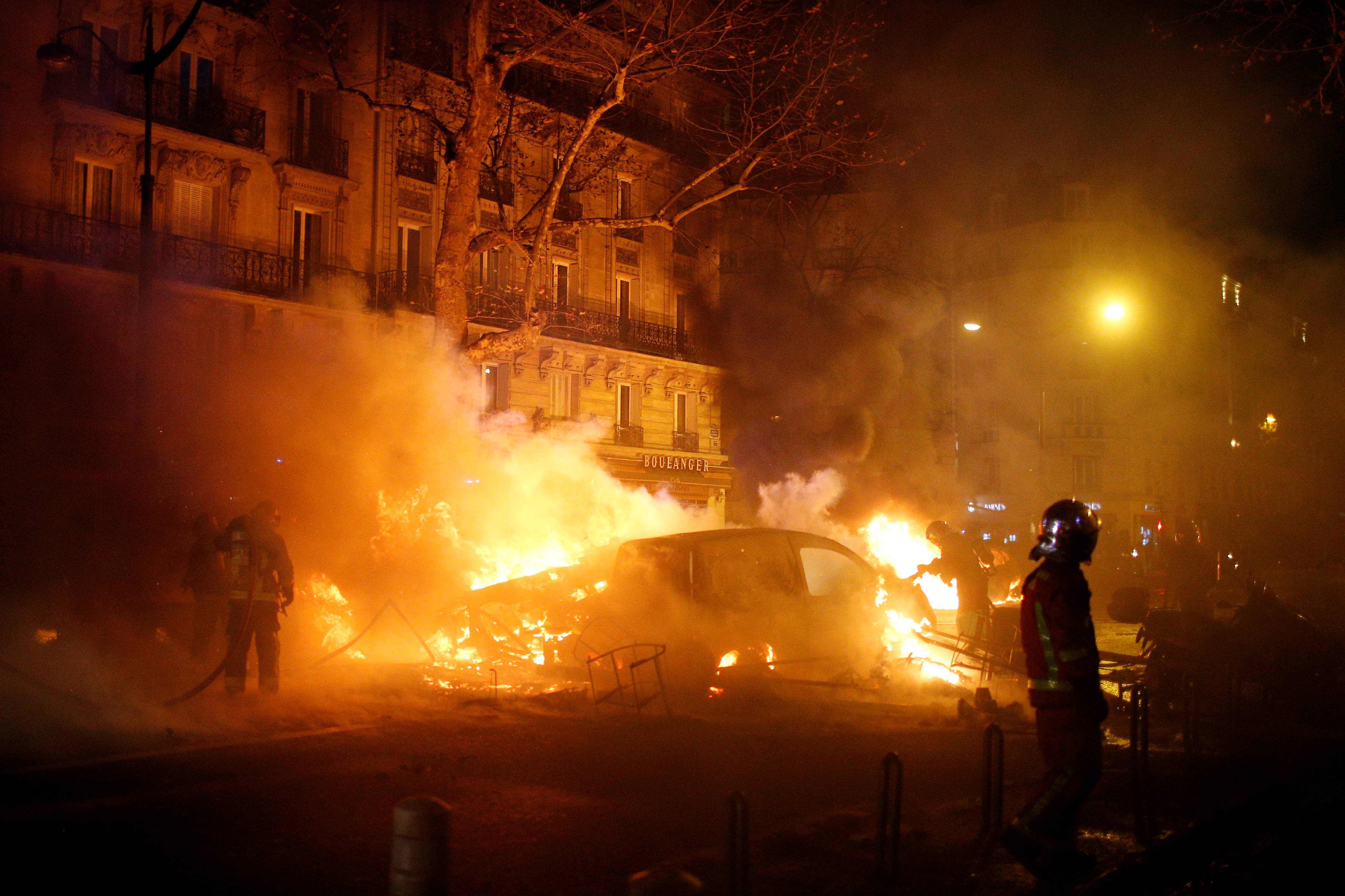 Firemen extinguish burning cars set afire by protesters wearing yellow vests, a symbol of a French drivers' protest against higher diesel fuel taxes, during clashes near the Place de l'Etoile in Paris
