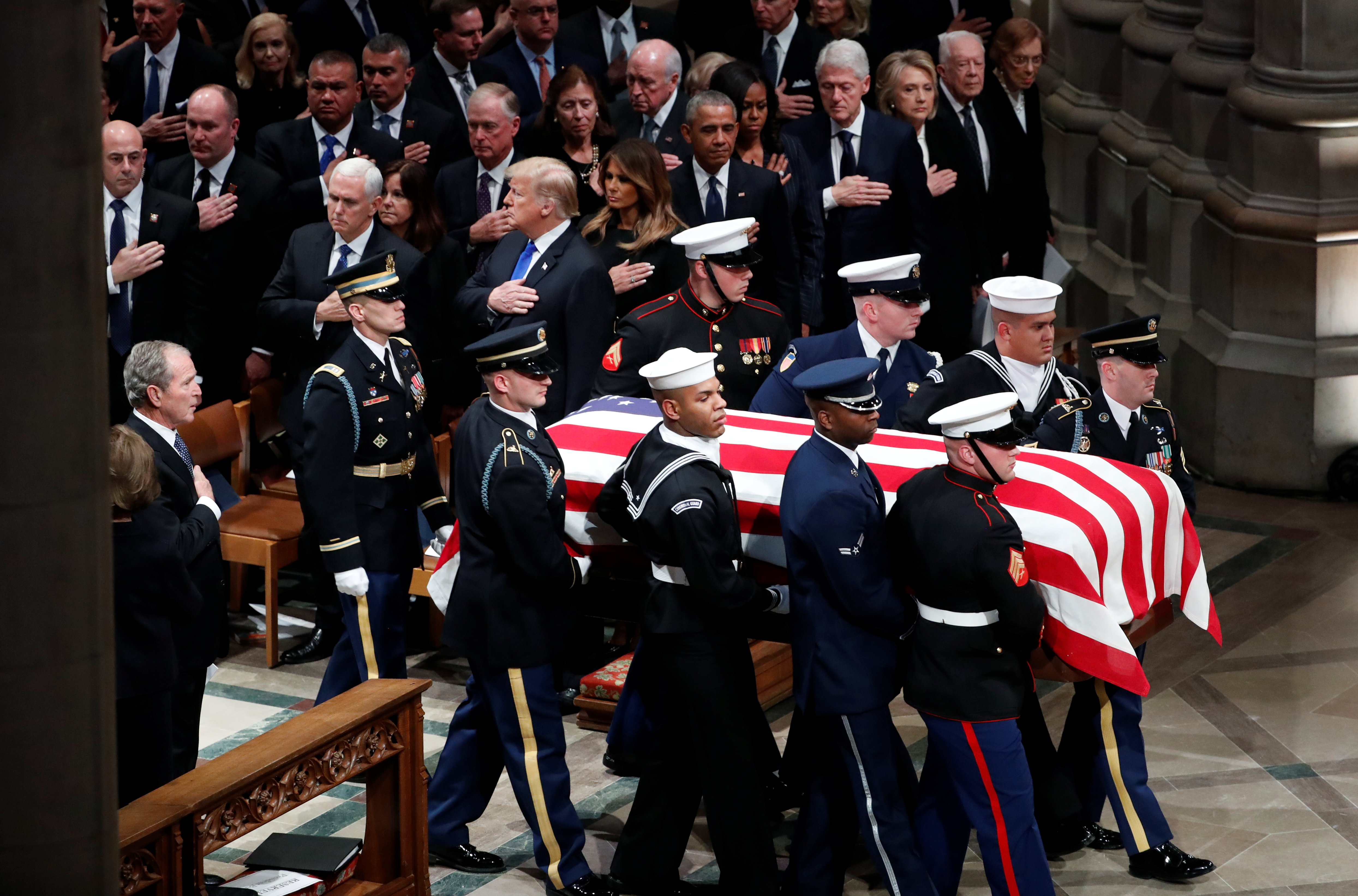 The flag-draped casket of former U.S. President George H.W. Bush is carried by military pallbearers past his son former President George W. Bush (L), U.S. President Donald Trump, first lady Melania Trump, former President Barack Obama, former first lady Michelle Obama, former President Bill Clinton, former first lady Hillary Clinton, former President Jimmy Carter and former first lady Rosalynn Carter as it arrives at his state funeral at Washington National Cathedral in Washington, U.S., December 5, 2018. REUTERS/Kevin Lamarque