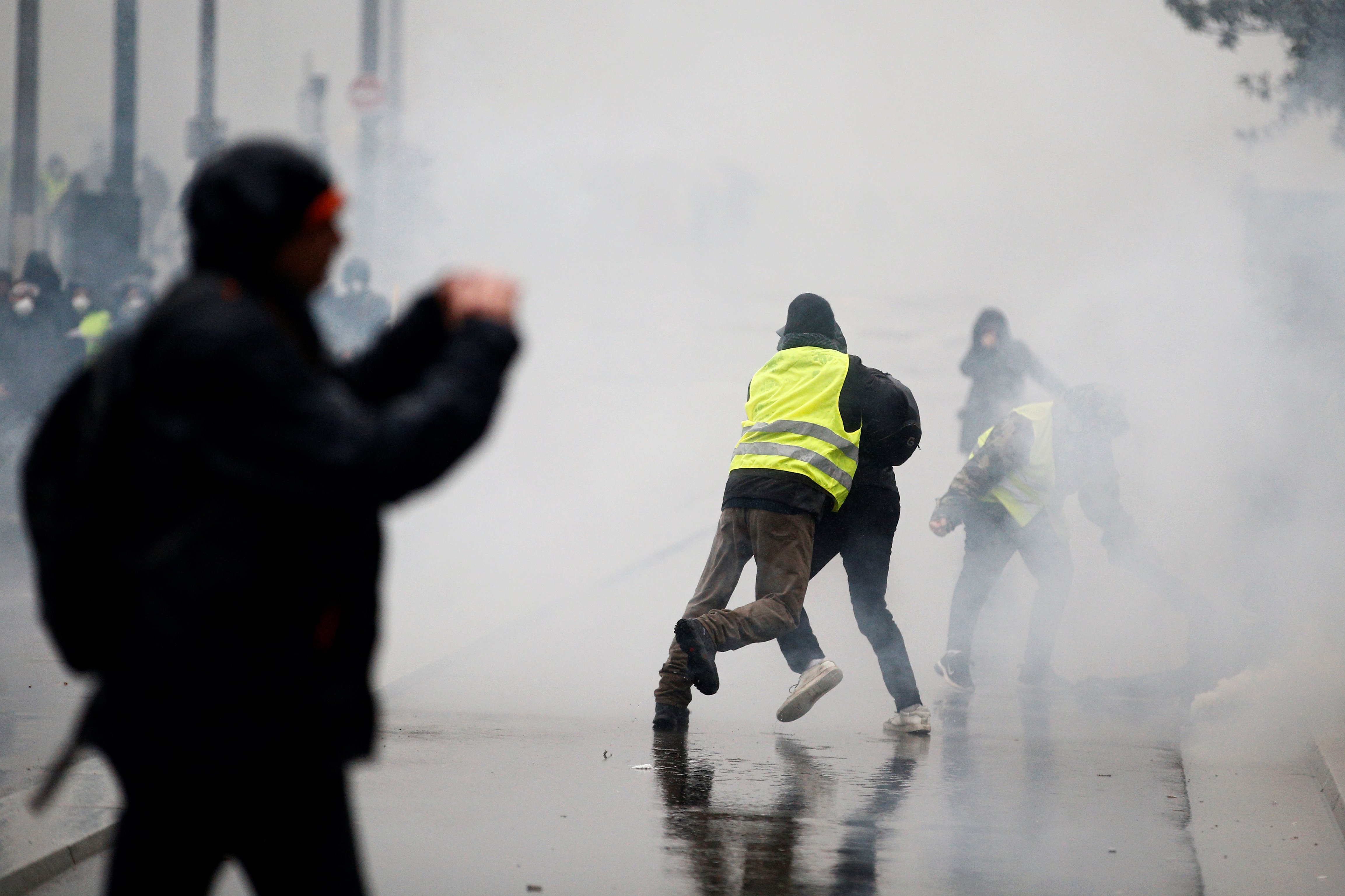 A man wearing a yellow vest tackles a protester as tear gas floats in the air during clashes with police at a demonstration by the "yellow vests" movement in Nantes, France, December 15, 2018. REUTERS/Stephane Mahe