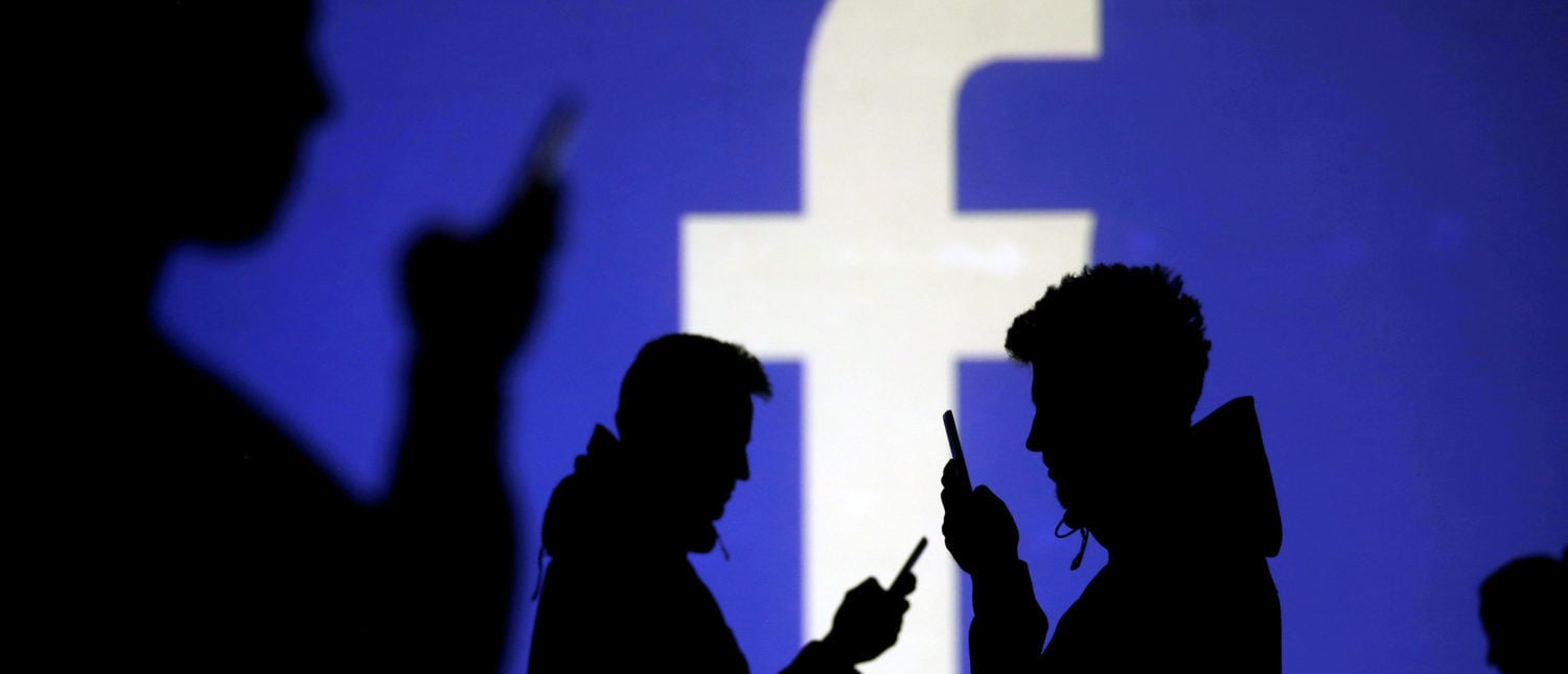 Silhouettes of mobile users are seen next to a screen projection of Facebook logo in this picture illustration taken March 28, 2018. REUTERS/Dado Ruvic/Illustration/File Photo - RC1D880ABF30