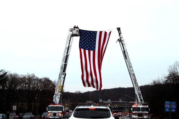 Ladder trucks from volunteer fire departments hoist a giant American flag above the honor escort for the family of Staff Sgt. Dylan Elchin as it merges on to Interstate 376 in Chippewa, Pennsylvania on Dec. 6, 2018. (Will Racke/TheDCNF)