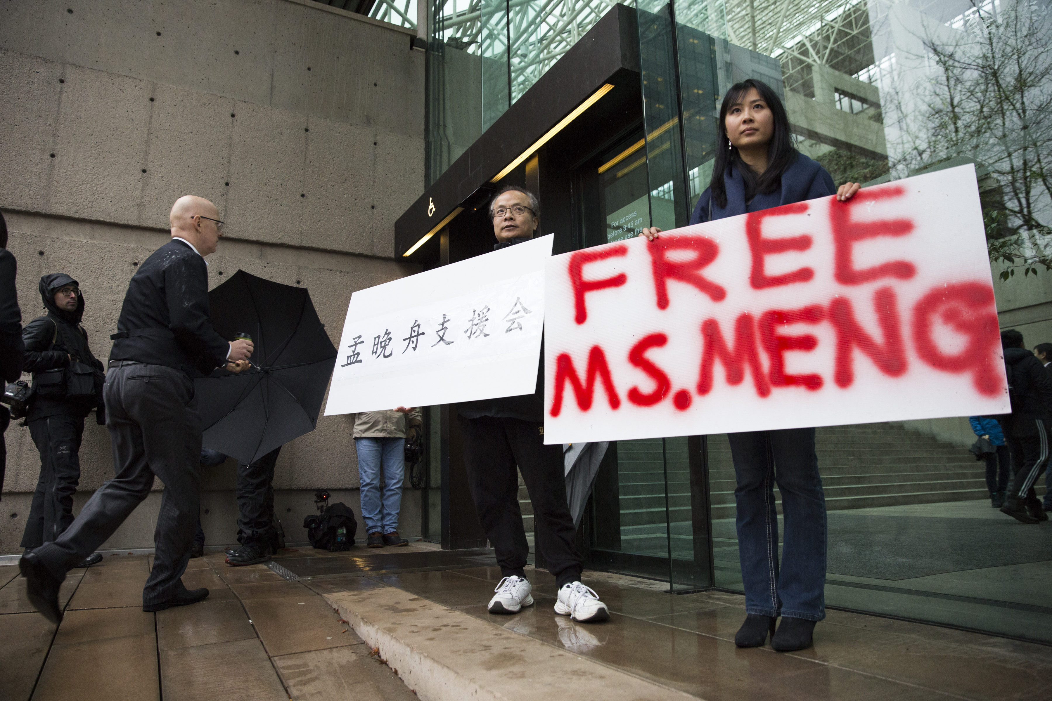 Robert Long (L) and Ada Yu hold signs in favor of Huawei Technologies Chief Financial Officer Meng Wanzhou outside her bail hearing at British Columbia Superior Courts following her December 1 arrest in Canada for extradition to the US, in Vancouver, British Columbia on December 11, 2018. (Photo by Jason Redmond / AFP) 