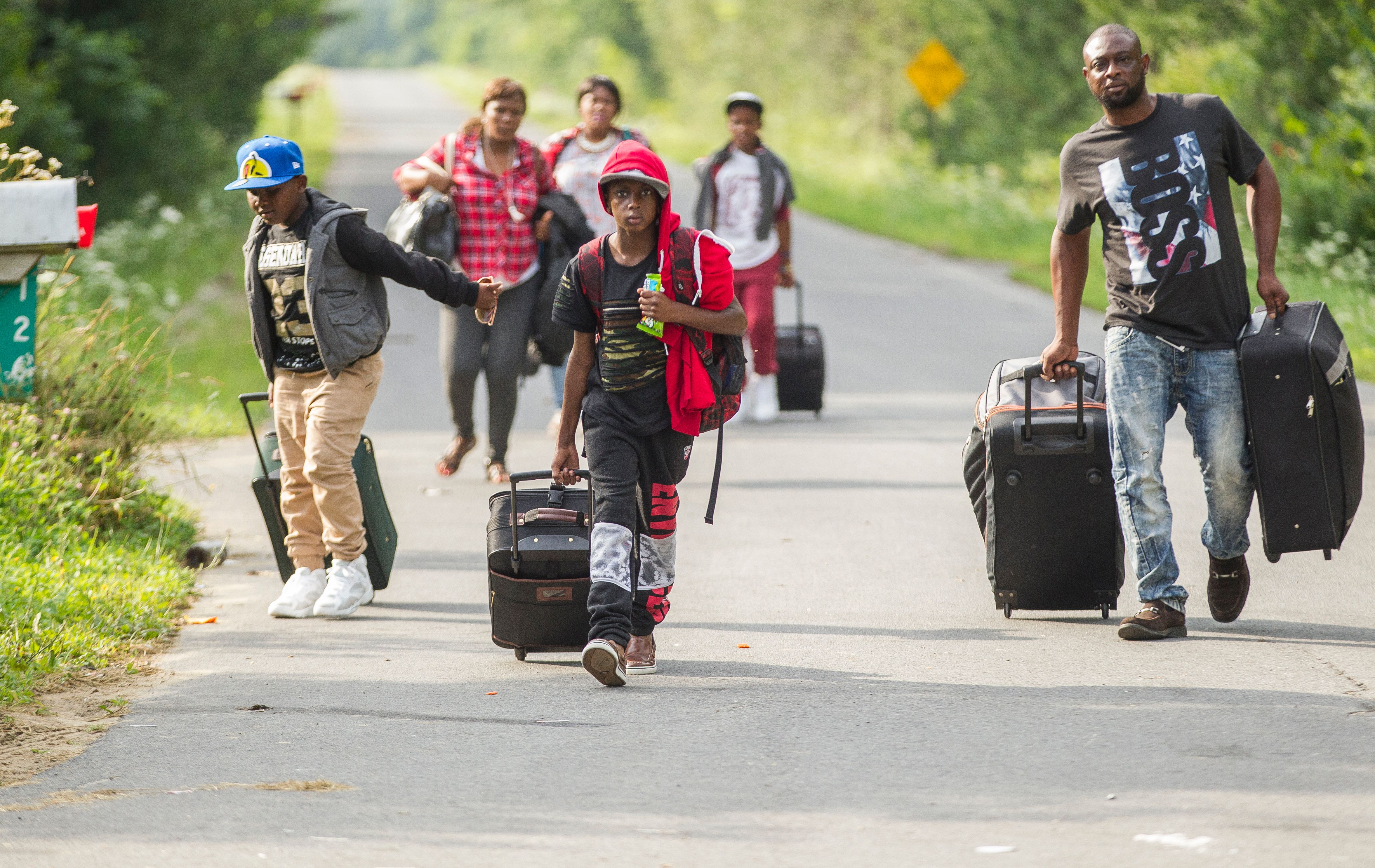 TOPSHOT - A group of people who claimed to be from Haiti walk down Roxham road in Champlain, New York as they prepare to cross the border into Canada illegally on August 4, 2017. Migrants have been crossing the border in greater numbers in recent weeks. / AFP PHOTO / Geoff Robins (Photo credit should read GEOFF ROBINS/AFP/Getty Images)