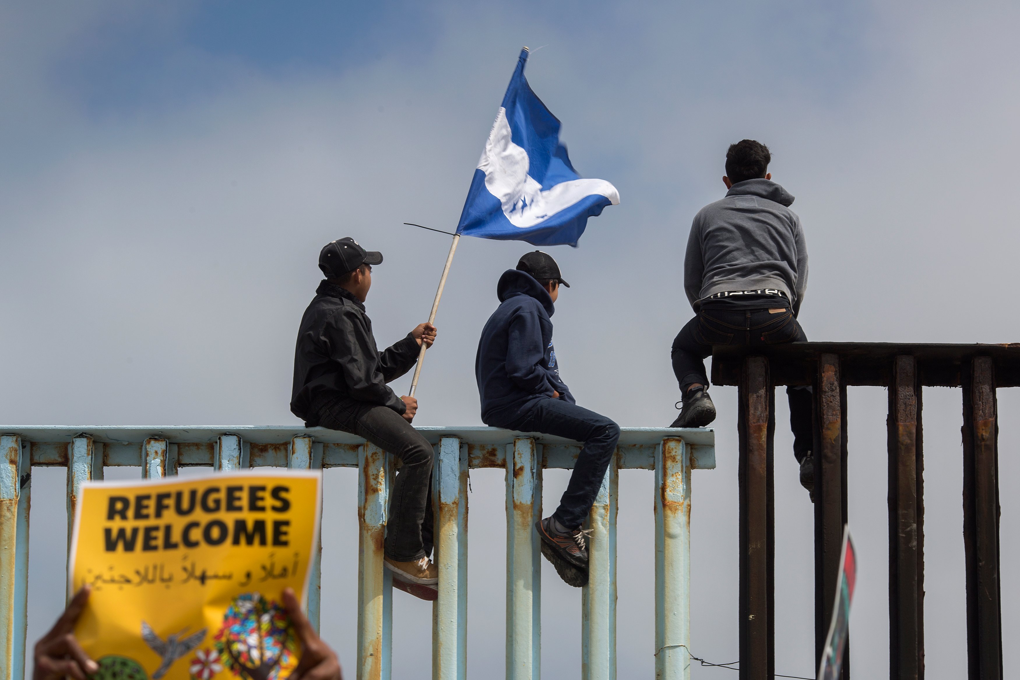 TIJUANA, MEXICO - APRIL 29: People hold a Honduran flag and look into the United States from atop a section of border fence as members of a caravan of Central American asylum seekers arrive to a rally on April 29, 2018 in Tijuana, Baja California Norte, Mexico. More than 300 immigrants, the remnants of a caravan of Central Americans that journeyed across Mexico to ask for asylum in the United States, have reached the border to apply for legal entry. (Photo by David McNew/Getty Images)
