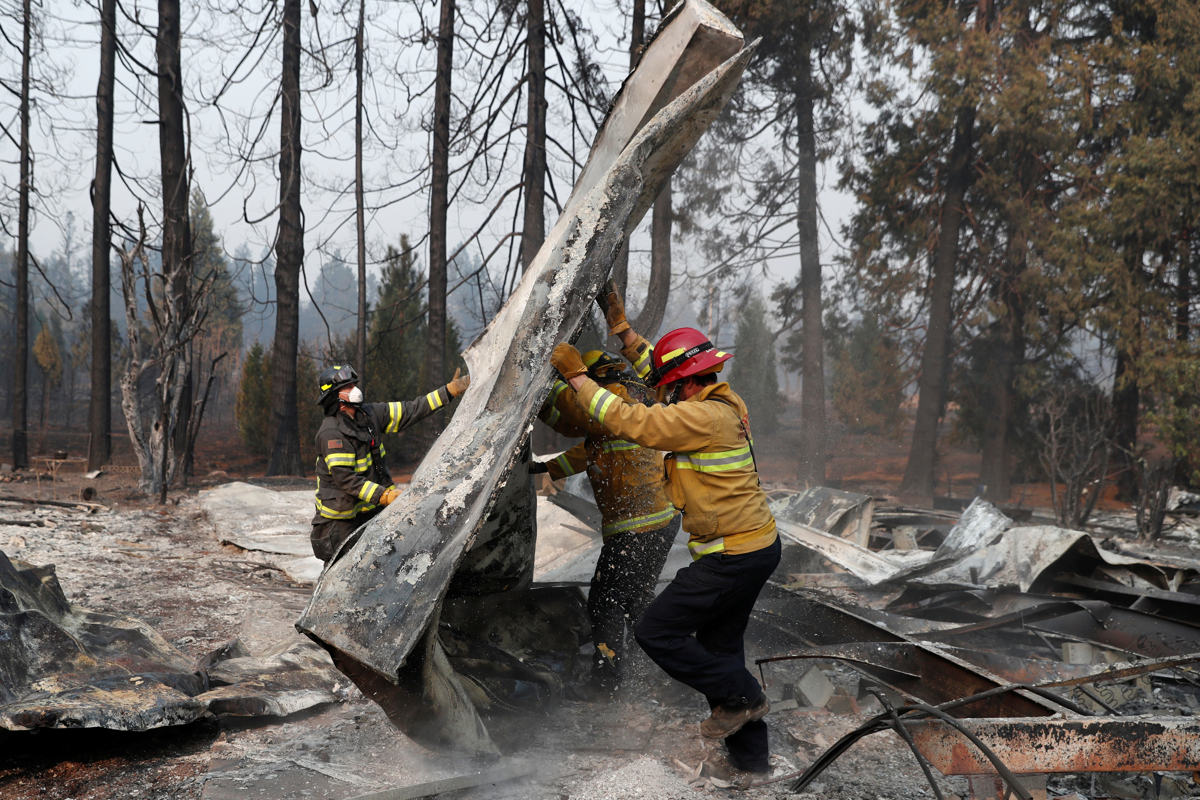 Firefighters move debris while recovering human remains from a trailer home destroyed by the Camp Fire in Paradise