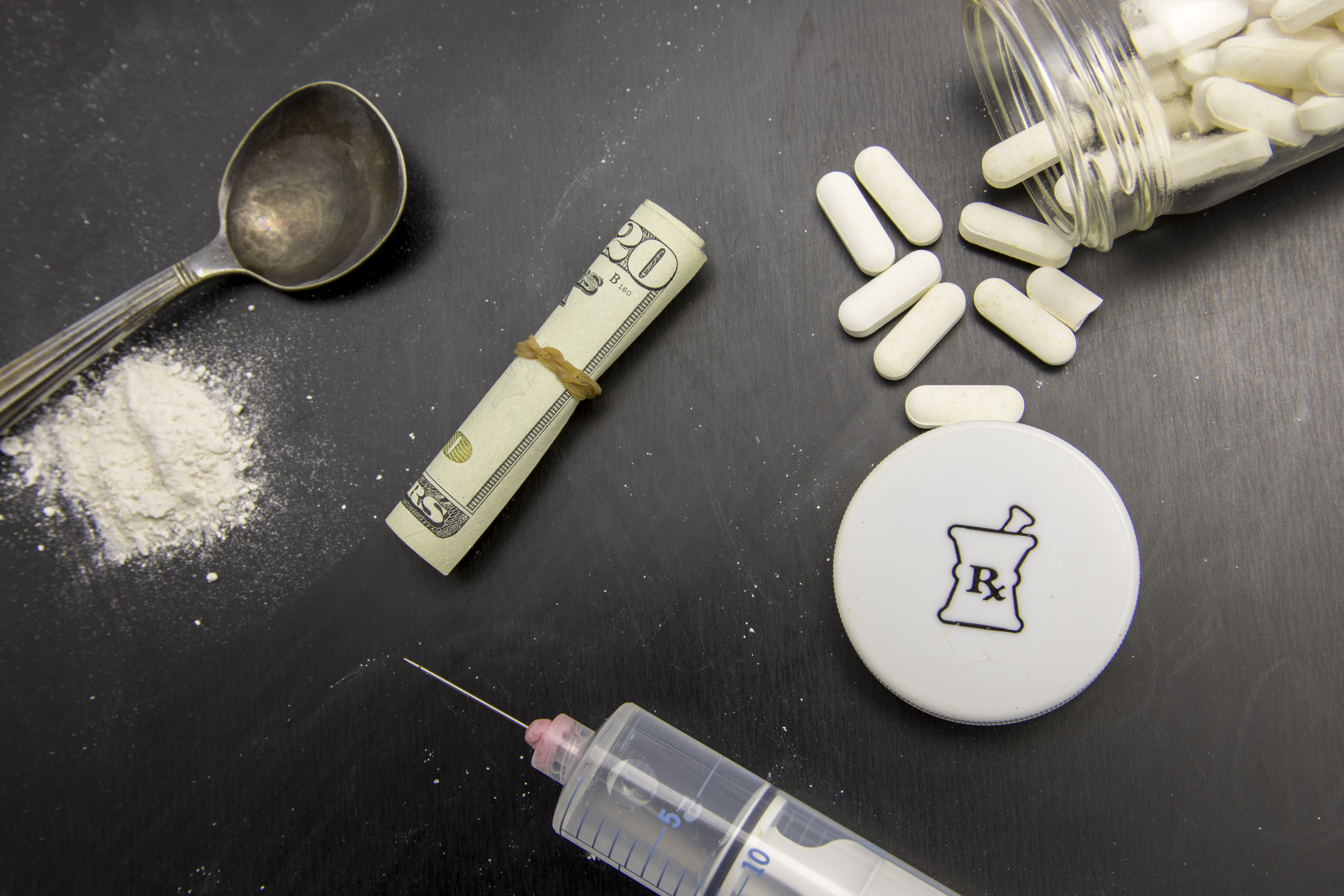 Opiods in pill, powder and syringe on chalkboard with rolled twenty dollar bills. (Shutterstock/ karenfoleyphotography)