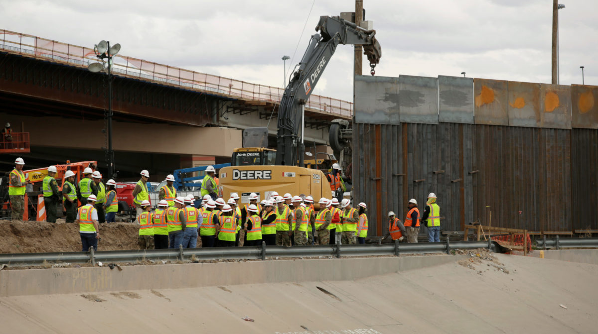 Workers and U.S border patrol officers stand next to an excavator working in a section of the new wall between El Paso and Ciudad Juarez