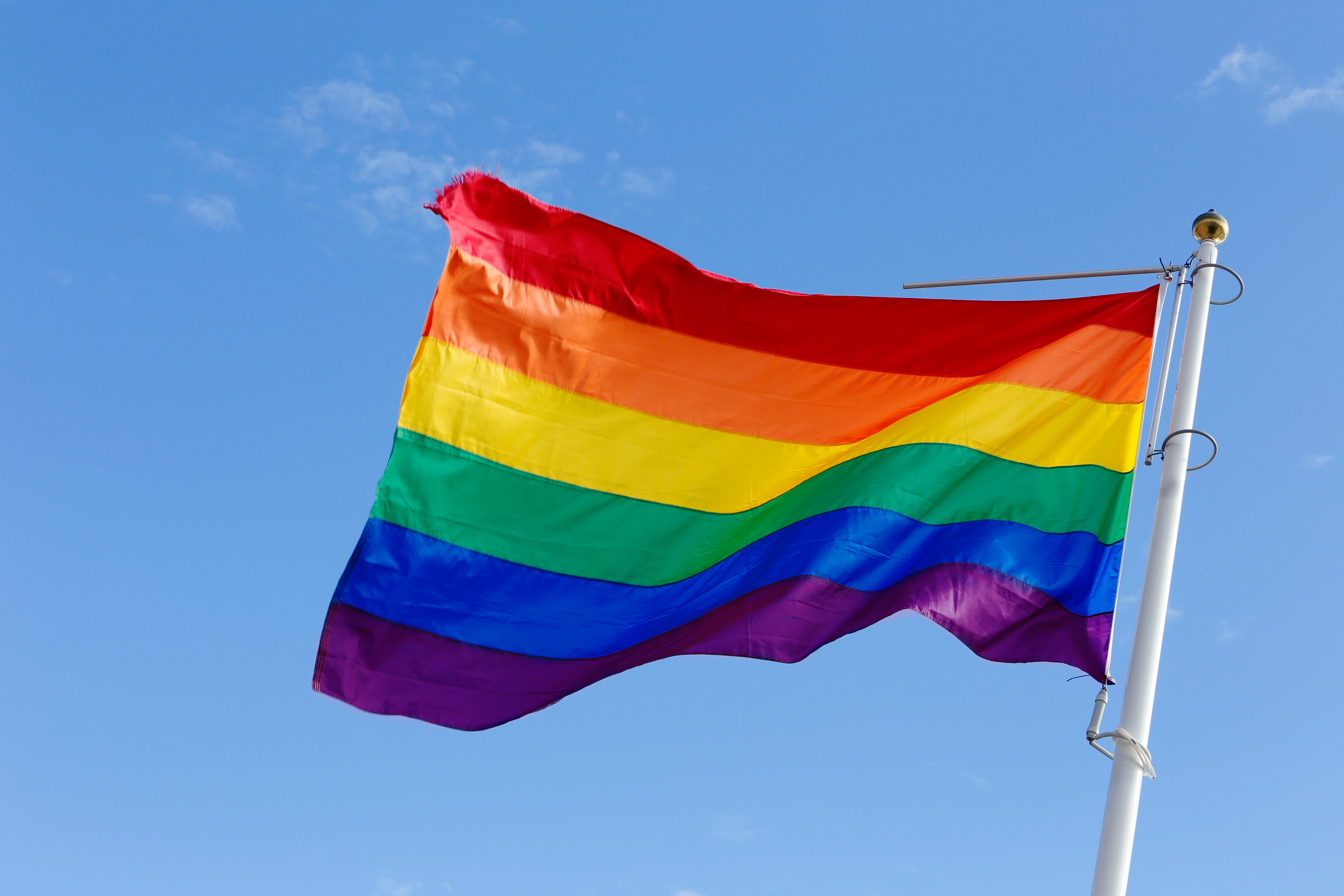 Closeup of a rainbow flag on blue sky. (Roland Magnusson/Shutterstock)