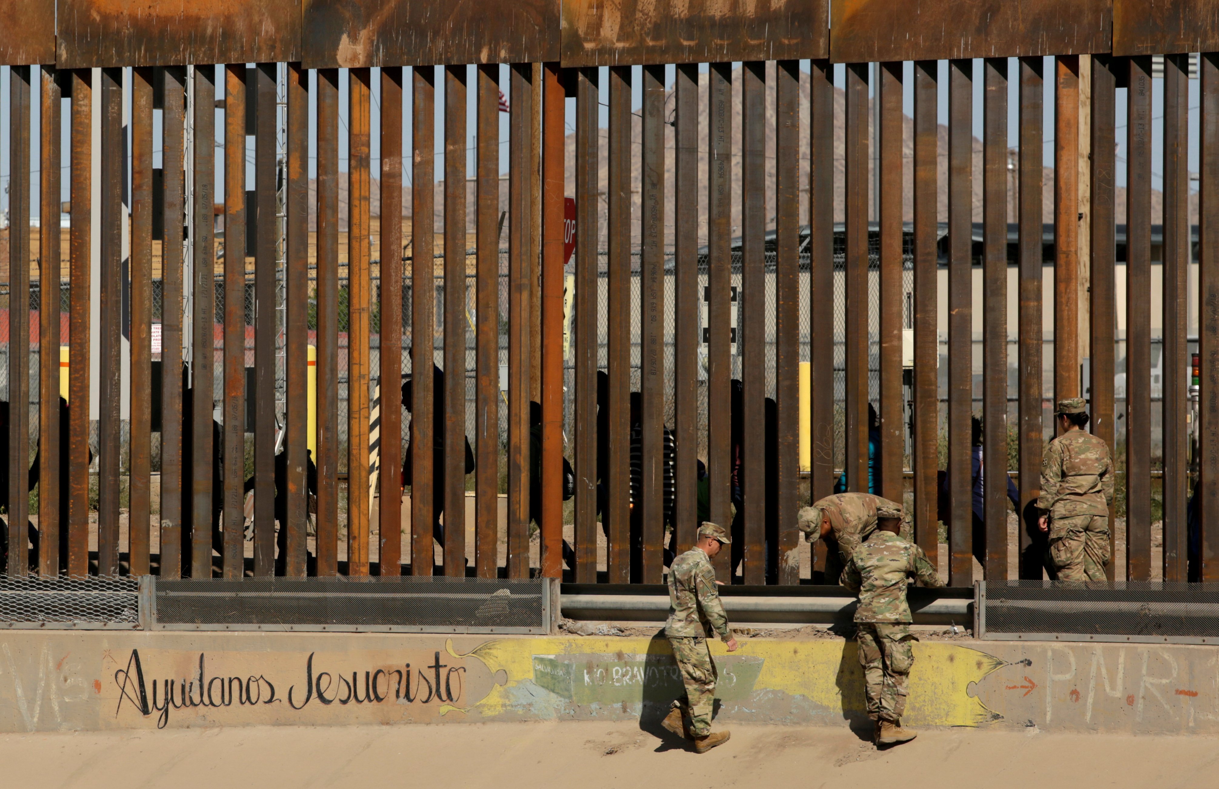 U.S. soldiers walk next to the border fence between Mexico and the United States, as migrants are seen walking behind the fence, after crossing illegally into the U.S. to turn themselves in, in El Paso, Texas, U.S., in this picture taken from Ciudad Juarez