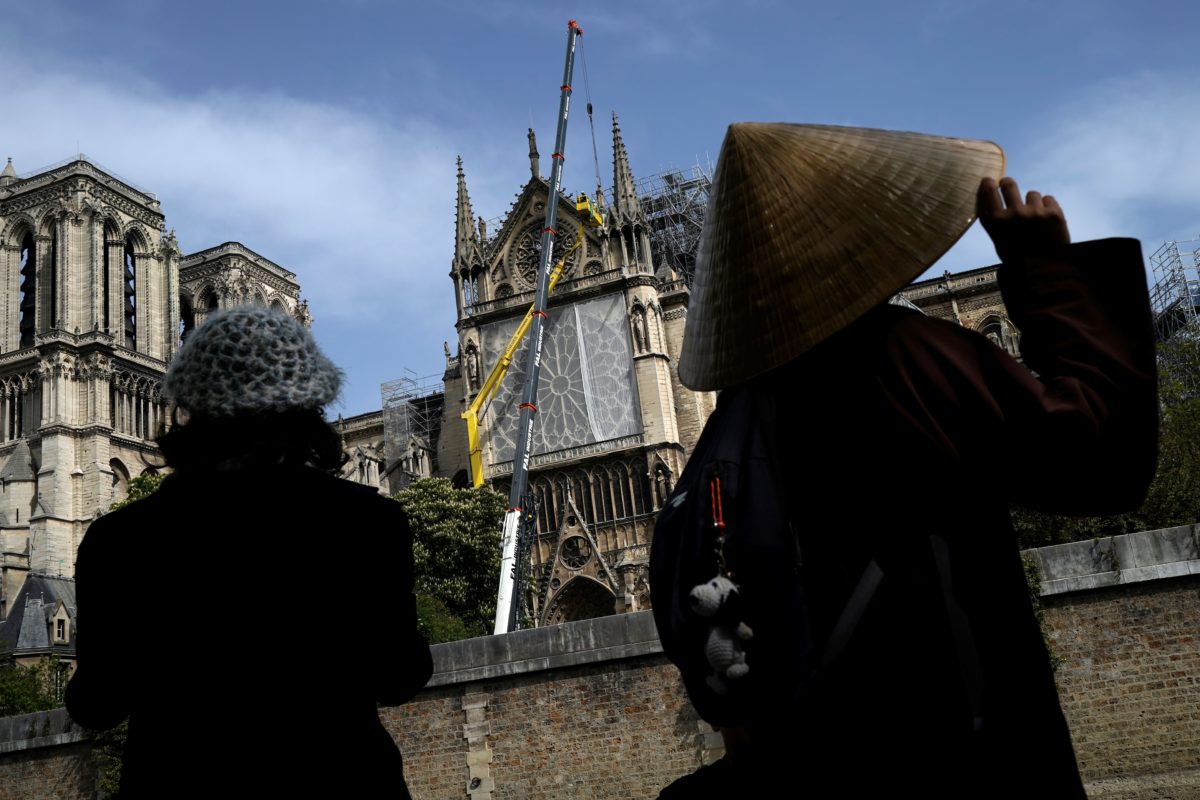 TOPSHOT - Bystanders look on as workers cover and protect the Rosette of Notre-Dame de Paris Cathedral in Paris on April 22, 2019, seven days after a fire devastated the cathedral.  (Photo credit  LIONEL BONAVENTURE/AFP/Getty Images)