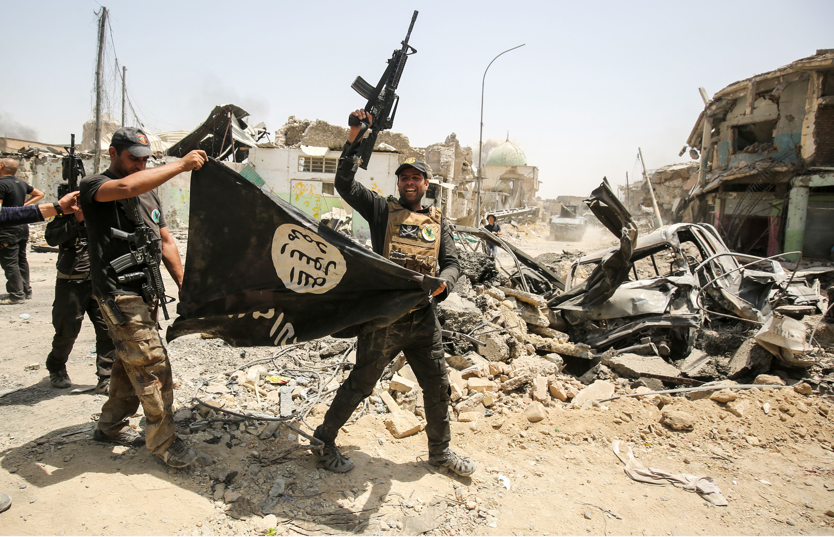 Members of the Iraqi Counter-Terrorism Service (CTS) cheer as they carry upside-down a black flag of the Islamic State (IS) group, with the destroyed Al-Nuri mosque seen in the background, in the Old City of Mosul on July 2, 2017, during the offensive to retake the city from IS fighters.