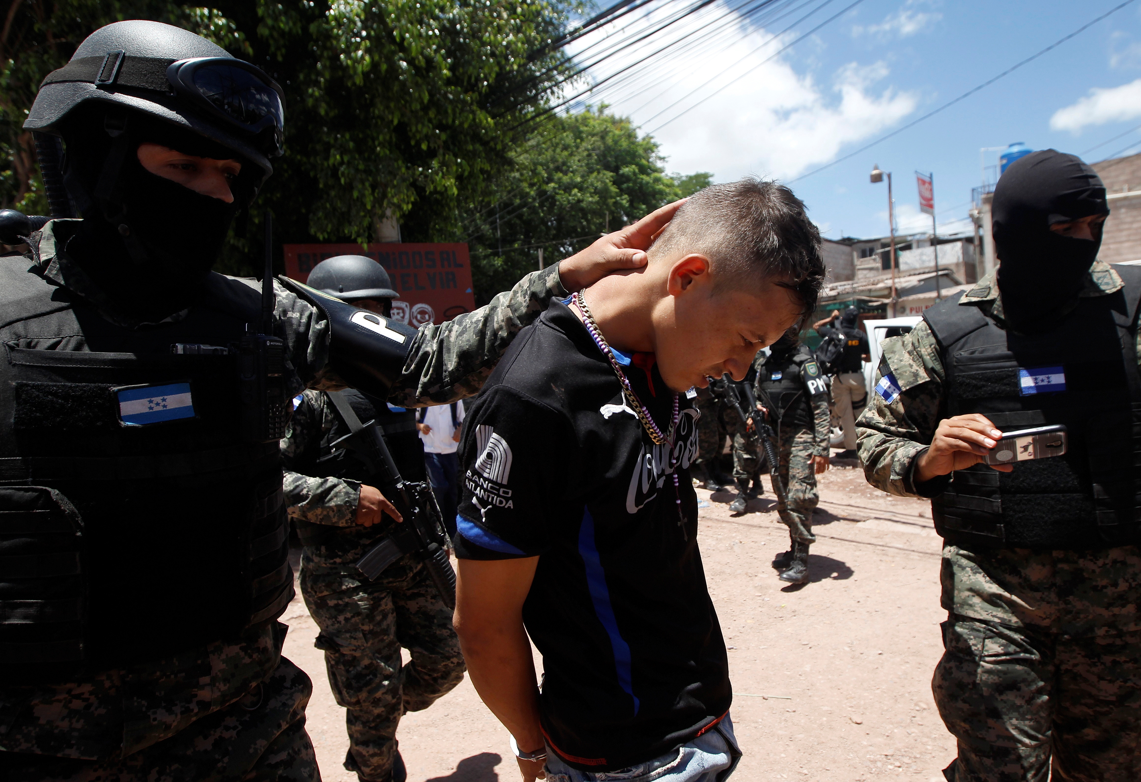 Military policemen escort a suspected MS-13 gang member detained during Operation Hunter, before taking him to police facilities for an investigation on a clandestine mass grave where the gang buried their victims, according to local media, in Tegucigalpa