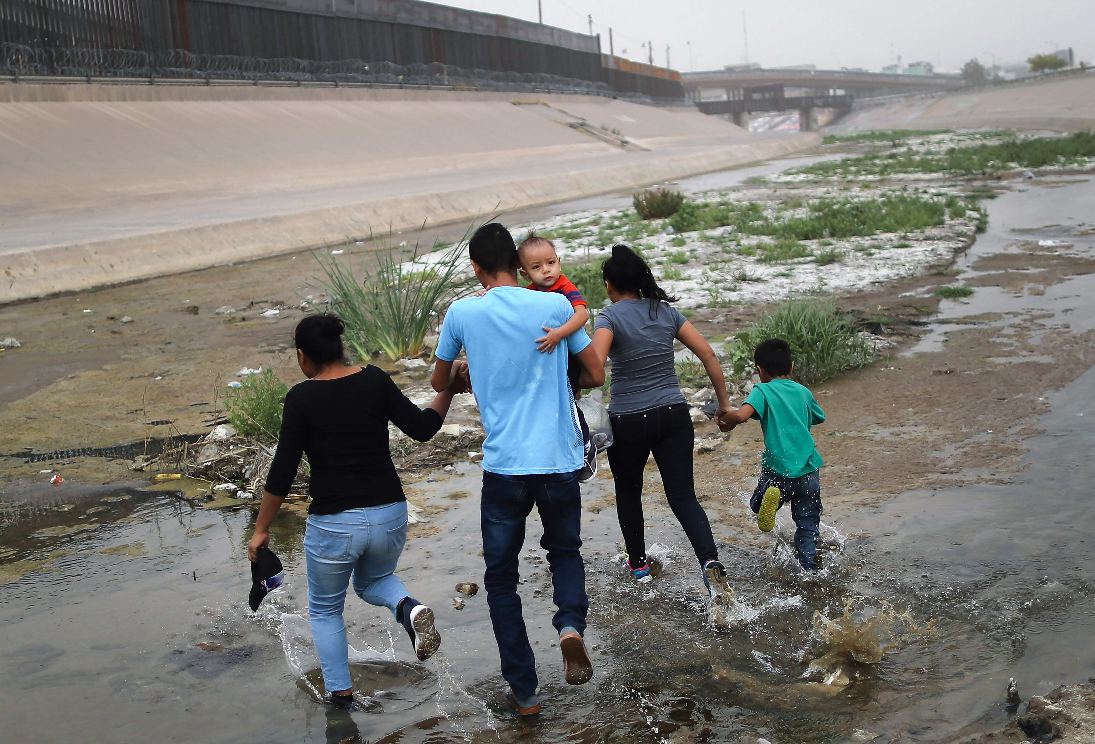 CIUDAD JUAREZ, MEXICO - MAY 20: Migrants hold hands as they cross the border between the U.S. and Mexico at the Rio Grande river, on their way to enter El Paso, Texas, on May 20, 2019 as taken from Ciudad Juarez, Mexico. The location is in an area where migrants frequently turn themselves in and ask for asylum in the U.S. after crossing the border. Approximately 1,000 migrants per day are being released by authorities in the El Paso sector of the U.S.-Mexico border amidst a surge in asylum seekers arriving at the Southern border.