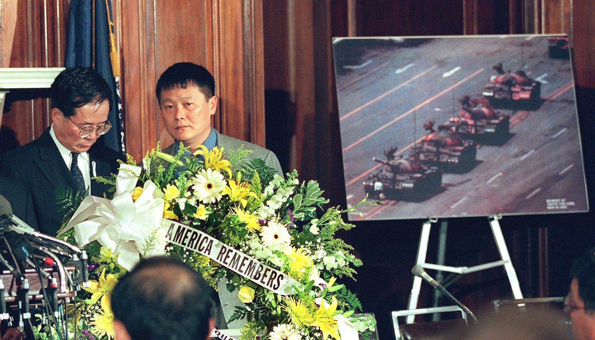 Former Chinese dissidents Harry Wu (L) and Wei Jingsheng (R) stand behind a wreath and next to the photo of a man standing in front of Chinese tanks during the Tiananmen Square Massacre during ceremonies June 4 on Capitol Hill marking the ninth anniversary of the event in Washington, DC. (LUKE FRAZZA/AFP/Getty Images)