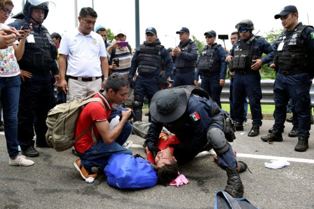 A federal police officer checks the head of an injured migrant during a joint operation by the Mexican government to stop a caravan of Central American migrants on their way to the U.S., at Metapa de Dominguez, in Chiapas state, Mexico June 5, 2019. REUTERS/Jose Torres
