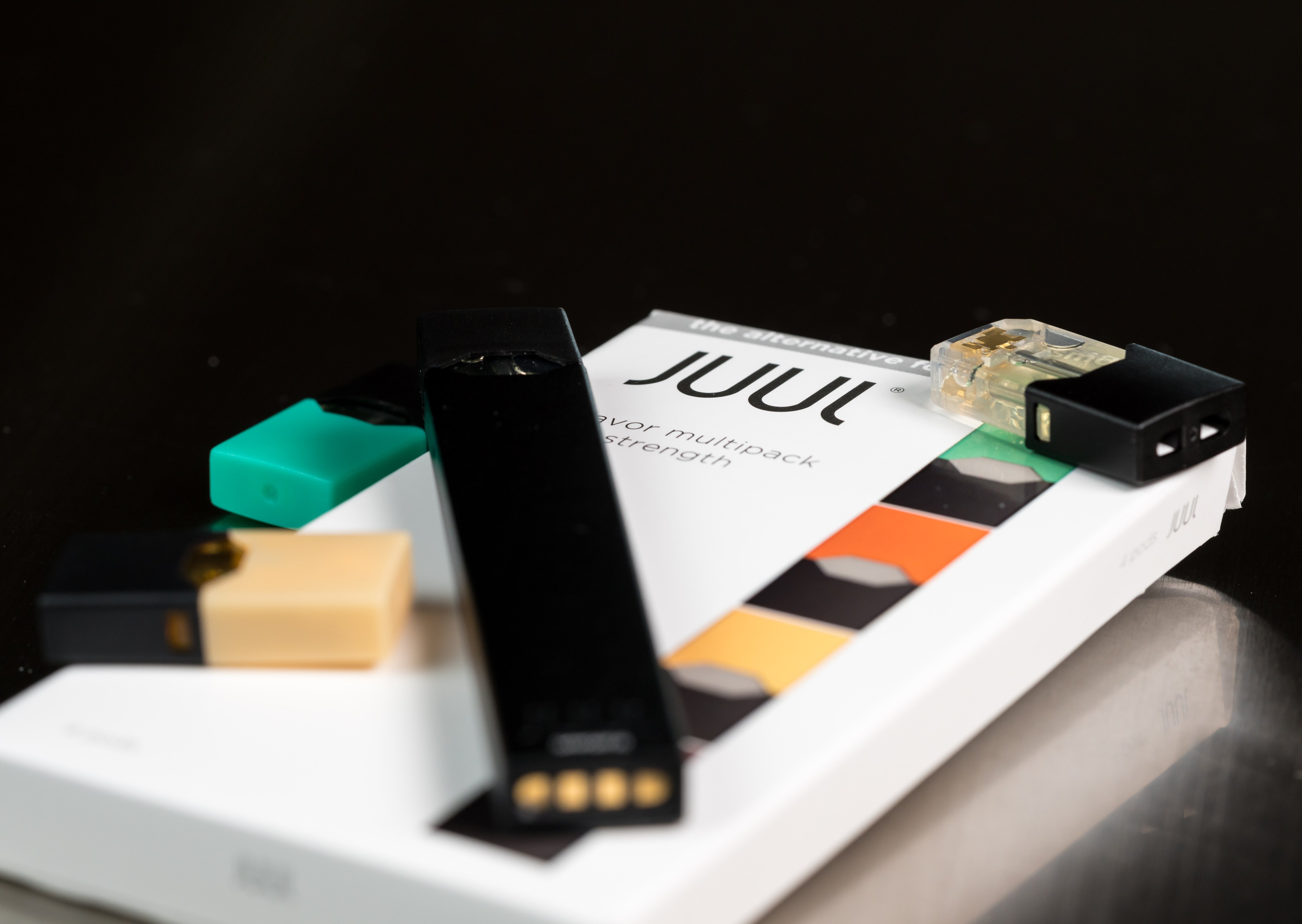 A Juul e-cigarette or nicotine vapor dispenser box and JUULpod rest against a dark background. Shutterstock image via Steve Heap