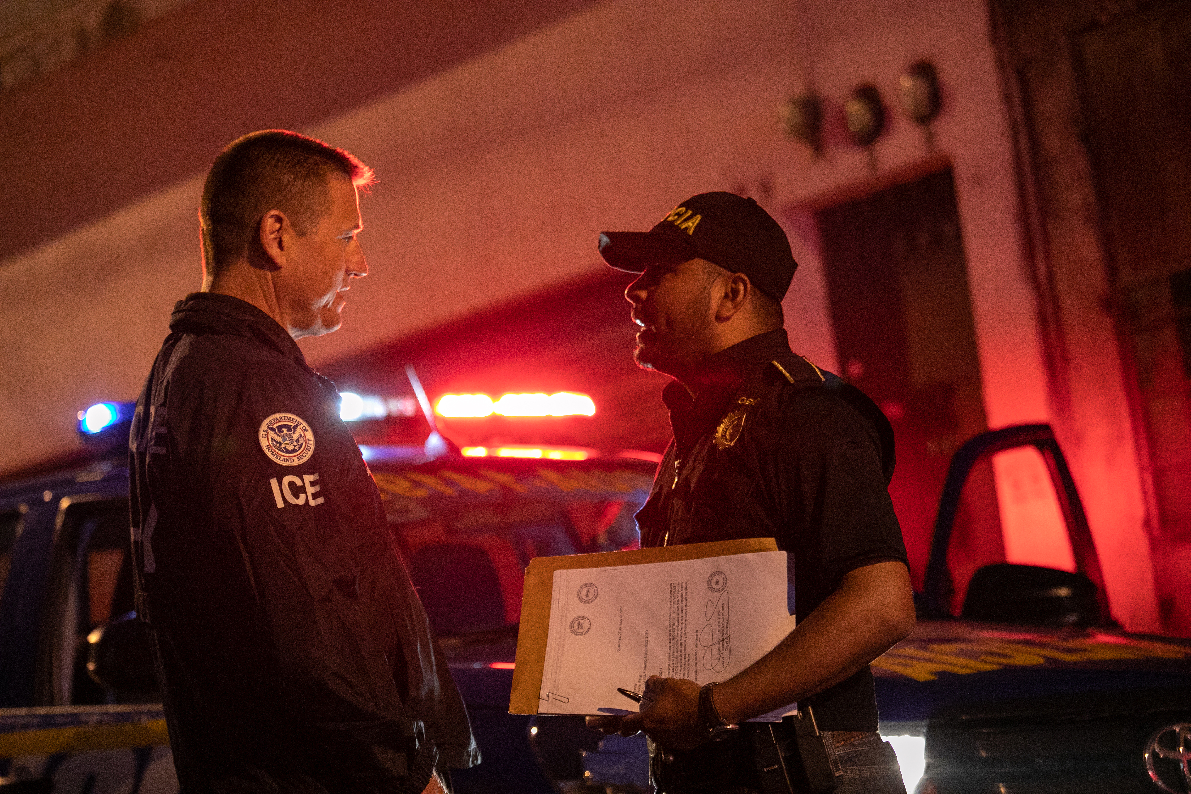 GUATEMALA CITY, GUATEMALA - MAY 29: An ICE agent with U.S. Homeland Security Investigations (HSI), (L) and a Guatemalan policeman speak at the scene of a raid where a suspected human trafficker was taken into custody on May 29, 2019 in Guatemala City. Homeland Security agents accompanied Guatemalan police on an early morning raid, the first since Acting U.S. Homeland Security Secretary Kevin McAleenan signed an agreement with his Guatemalan counterparts, increasing cooperation on human and drug smuggling. McAleenan is on a four-day trip to Guatemala. (Photo by John Moore/Getty Images)