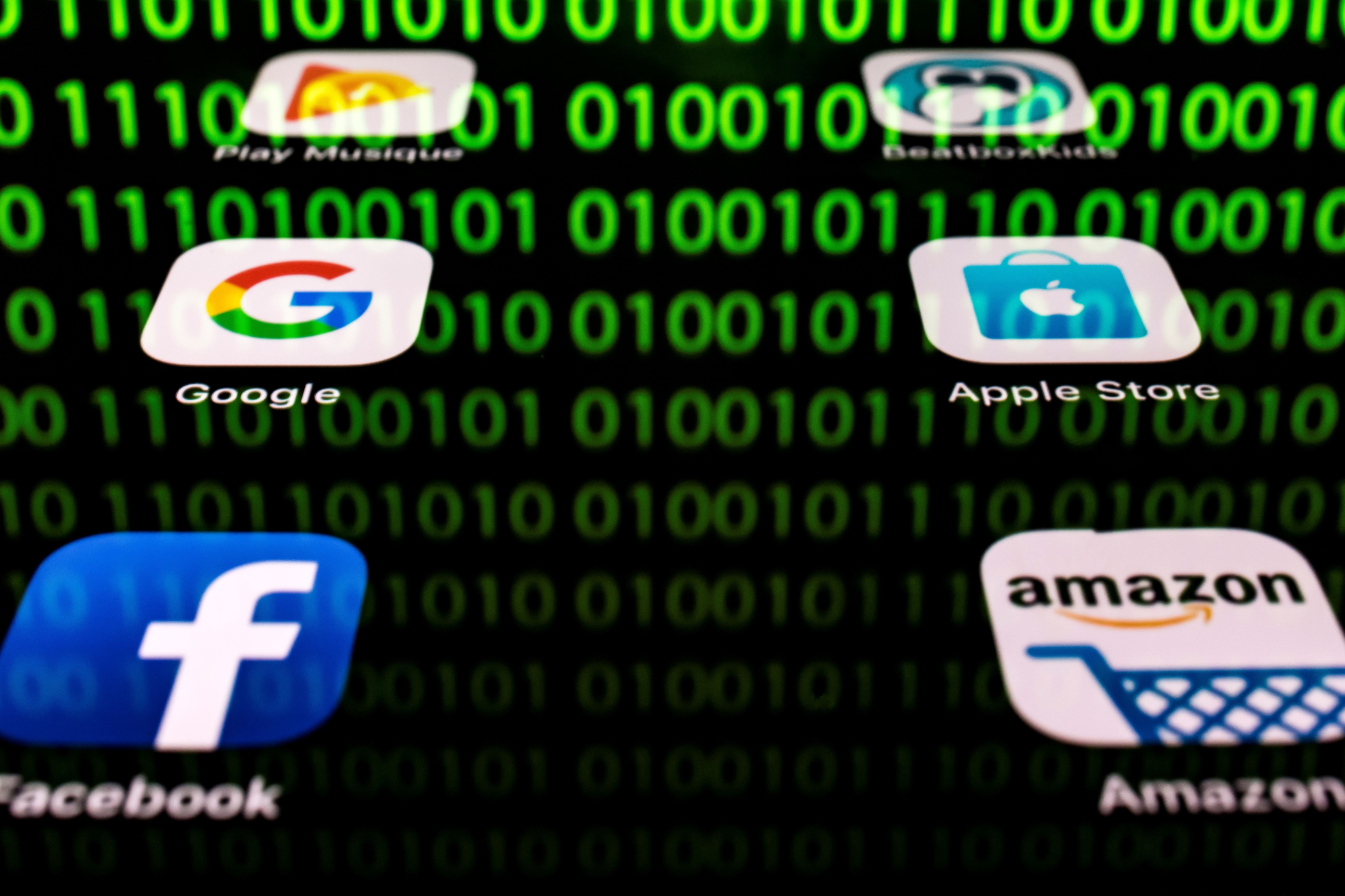 This illustration picture taken on April 20, 2018 in Paris shows apps for Google, Amazon, Facebook, Apple (GAFA) and the reflexion of a binary code displayed on a tablet screen. (LIONEL BONAVENTURE/AFP/Getty Images)