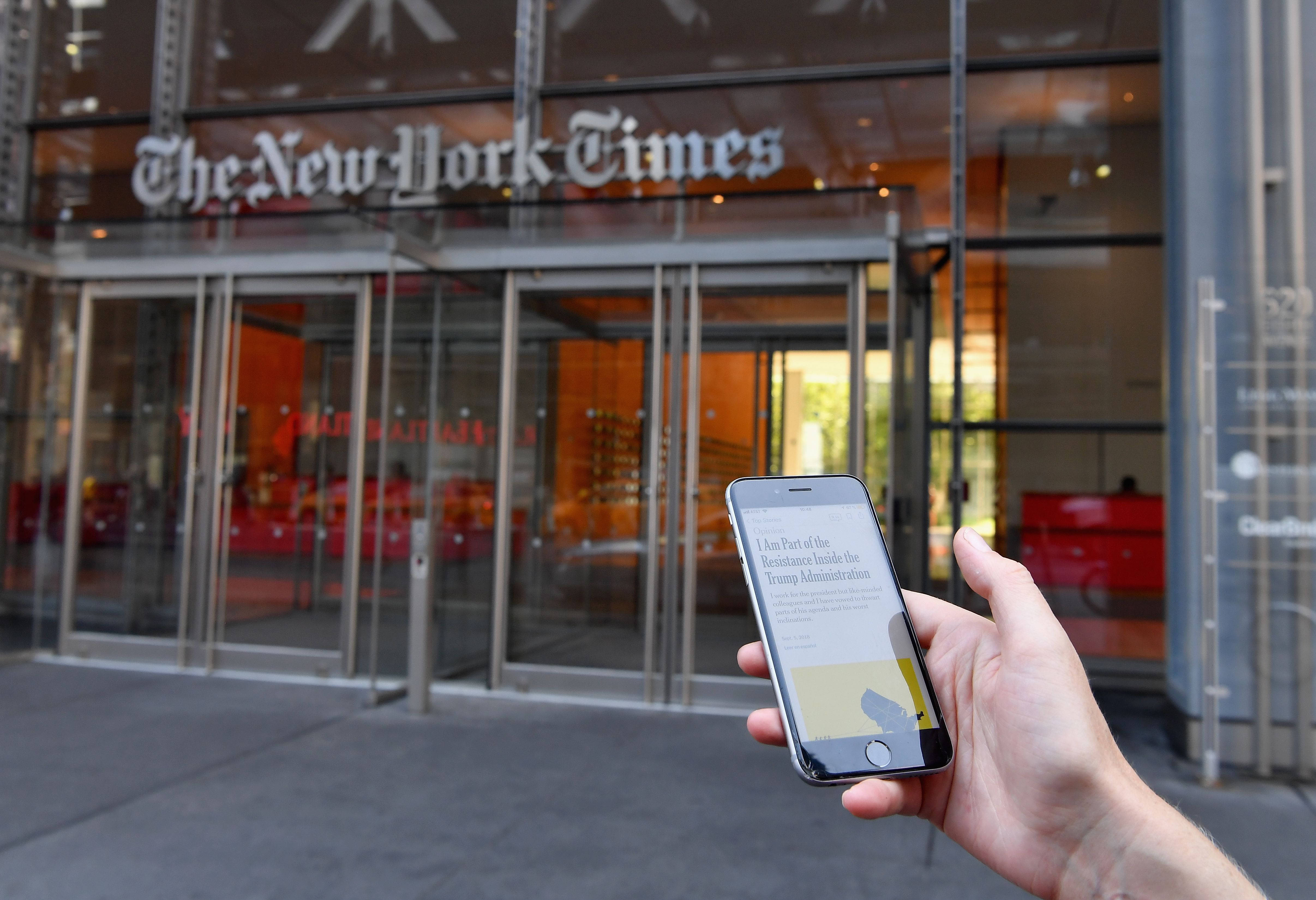 A smartphone displaying a New York Times opinion piece titled "I Am Part of the Resistance Inside the Trump Administration" is held up in this illustration in front of the New York Times building on September 6, 2018 in New York. (Photo by ANGELA WEISS / AFP/ Getty Images)