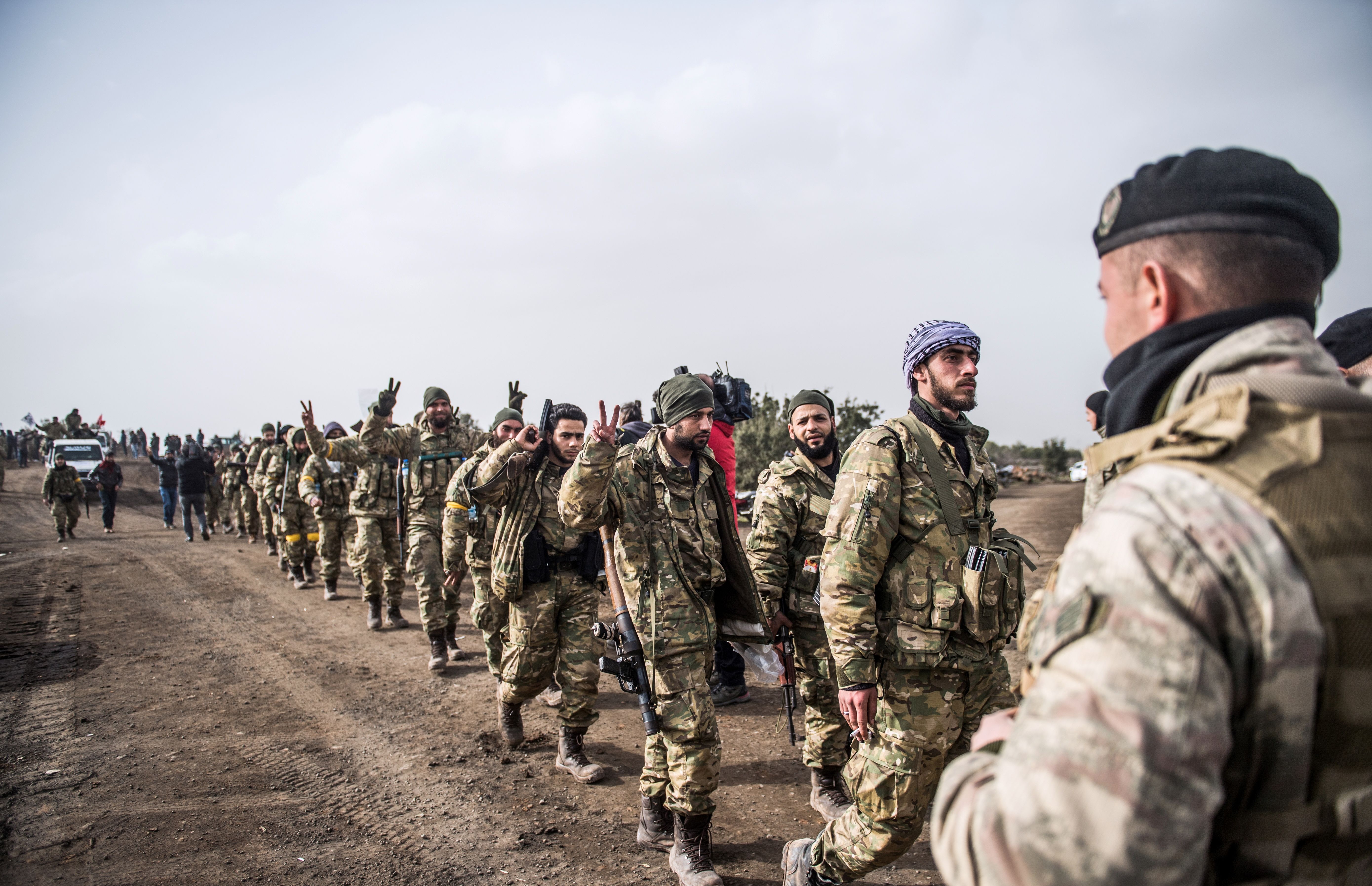 Syrian opposition fighters walk through Syria in front of Turkish troops near the Syrian border at Hassa, Hatay province, on January 22, 2018. (Photo credit should read BULENT KILIC/AFP/Getty Images)