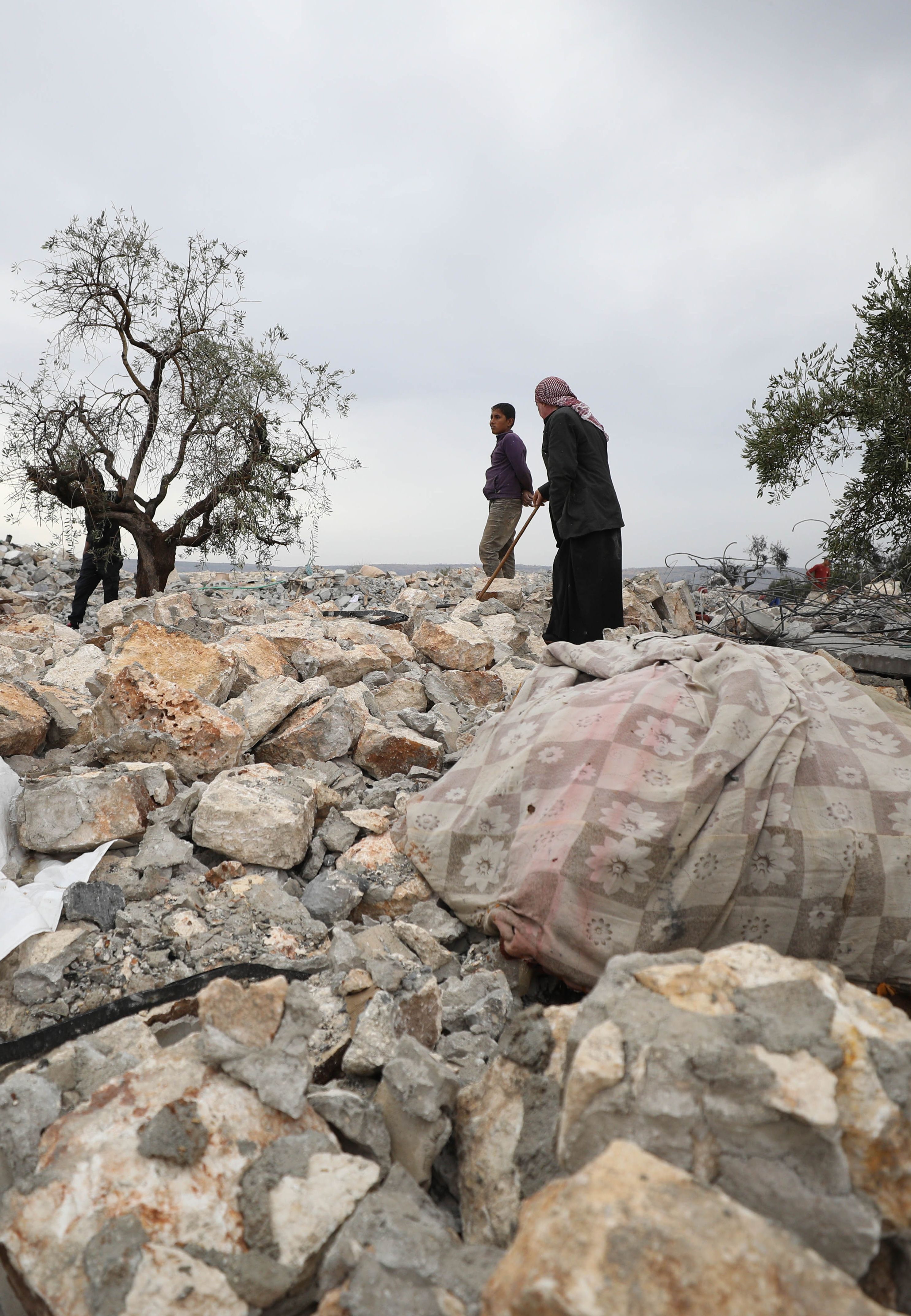 A picture taken on October 28, 2019 shows Syrians sifting through the rubble at the site of a suspected US-led operation against Islamic State (IS) chief Abu Bakr al-Baghdadi the previous day, on the edge of the small Syrian village of Barisha in the country's opposition-held northwestern Idlib province. - US President Donald Trump announced that Baghdadi, the elusive leader of the jihadist group and the world's most wanted man, was killed in the early hours of Octobe 27 in an overnight US raid near the village, located less than five kilometres from Turkey and controlled by the dominant jihadist group Hayat Tahrir al-Sham, an organisation that includes former operatives from Al-Qaeda's Syria affiliate. (Photo by Omar HAJ KADOUR / AFP) (Photo by OMAR HAJ KADOUR/AFP via Getty Images)