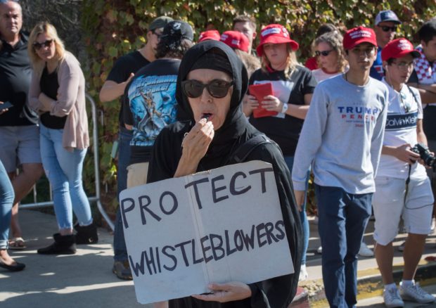 A Muslim woman holds a 'Protect Whistleblowers" sign as she walks past supporters of President Trump during a protest outside a book promotion by Donald Trump Jnr, at the UCLA campus in Westwood, California on November 10, 2019. (Photo by Mark RALSTON / AFP) (Photo by MARK RALSTON/AFP via Getty Images)