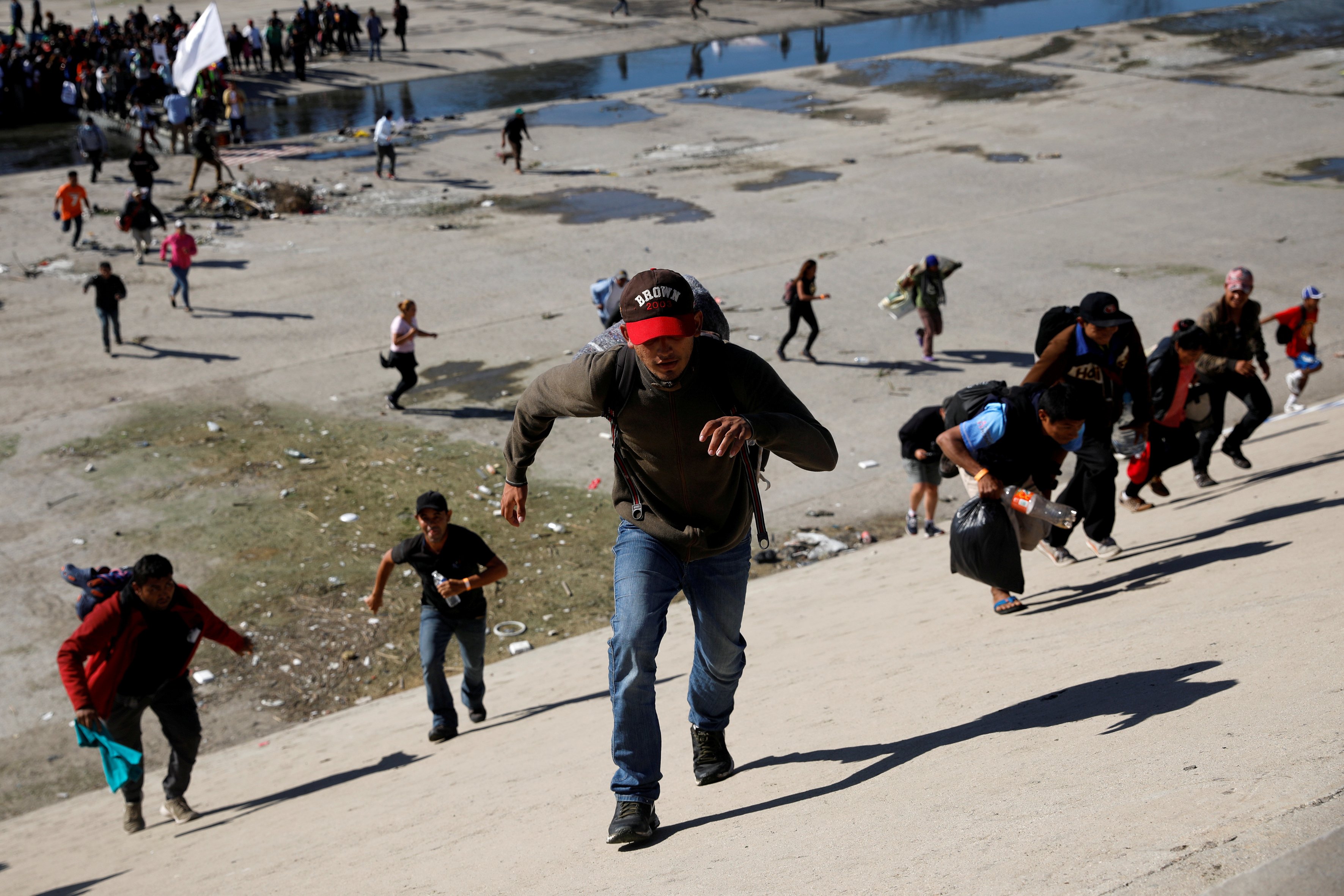 Migrants, part of a caravan of thousands traveling from Central America en route to the United States, run across the Tijuana river to reach the border wall between the U.S. and Mexico in Tijuana