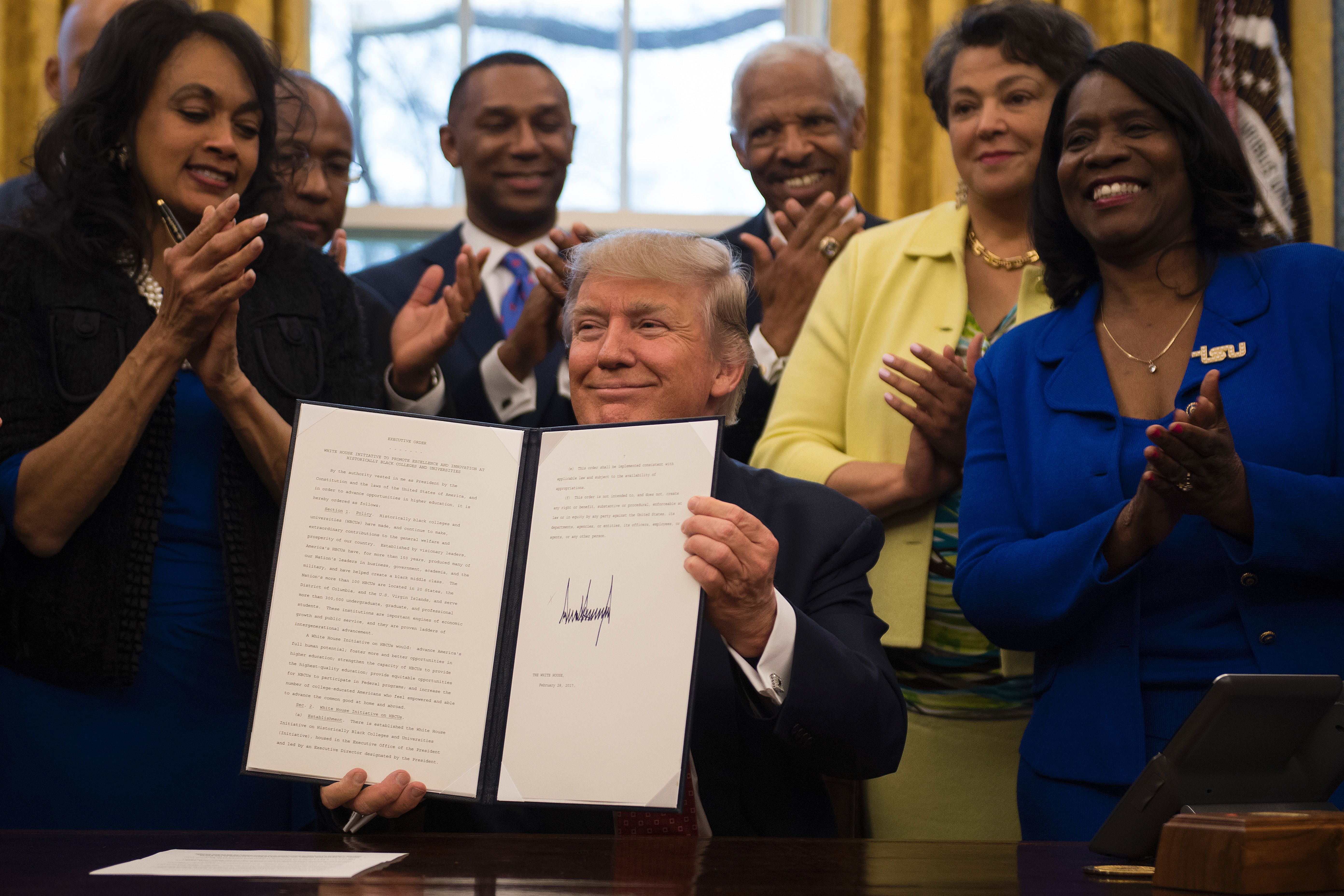 US President Donald Trump (C) holds up an executive order to bolster historically black colleges and universities (HBCUs) after signing it in the Oval Office of the White House in Washington, DC, February 28, 2017. / AFP / JIM WATSON (Photo credit should read JIM WATSON/AFP via Getty Images)