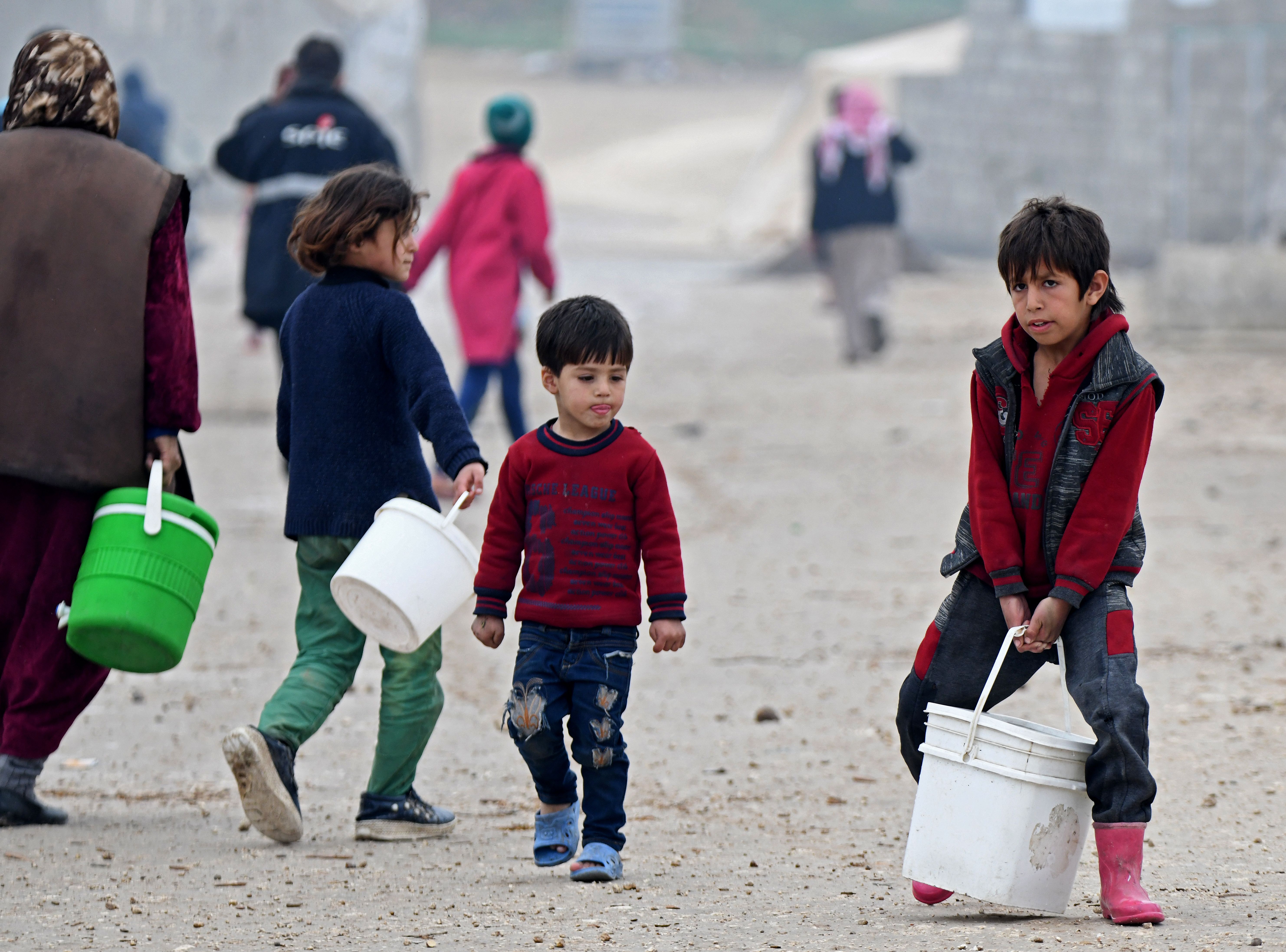 A displaced Syrian boy carries a bucket of humanitarian aid, consisting of heating material and drinking water, at a camp in the town of Mehmediye, near the town of Deir al-Ballut along the border with Turkey, on February 21, 2020. (Photo by RAMI AL SAYED/AFP via Getty Images)