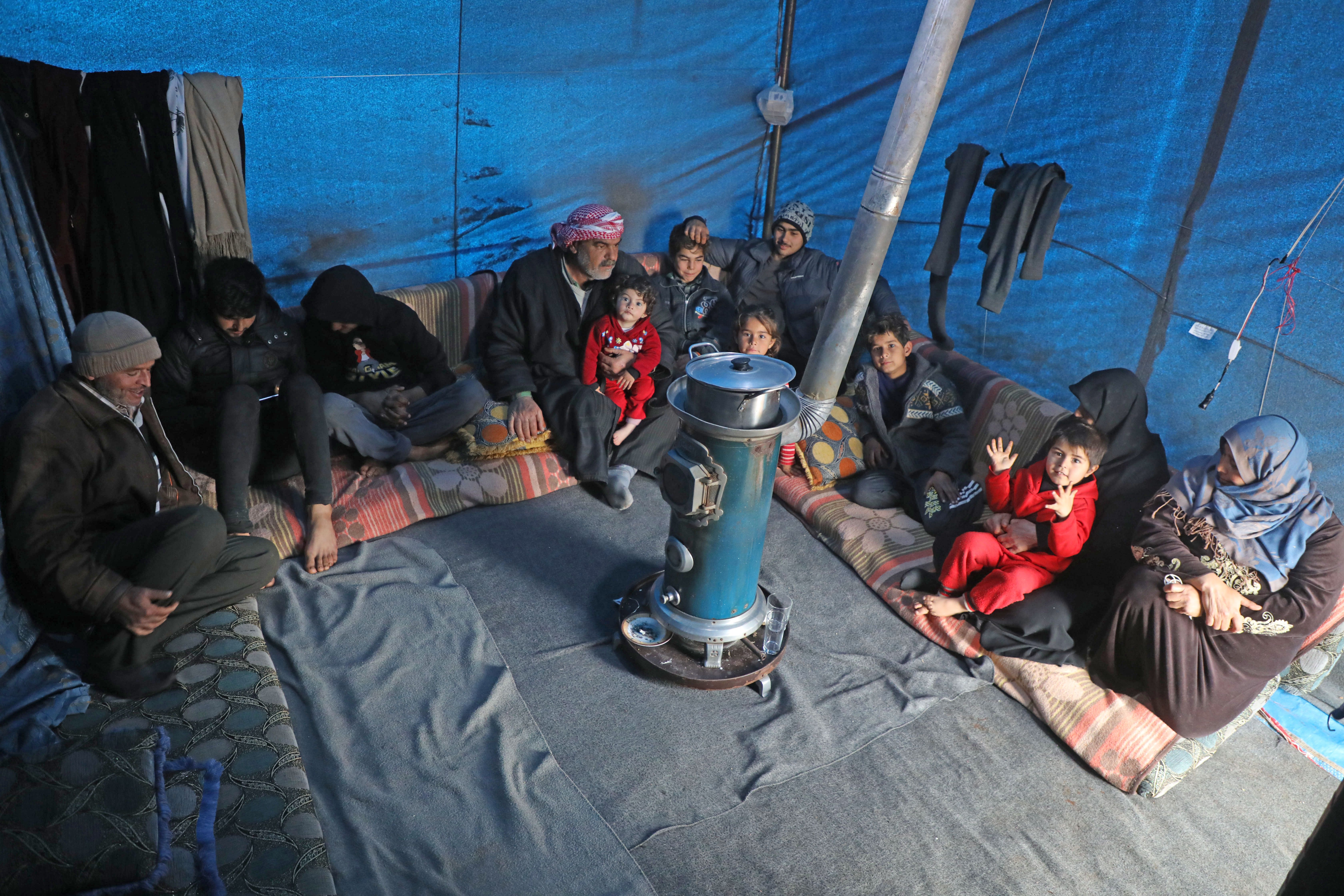 Syrian Abdel Razzak Sallat sit with his family inside a tent at an informal camp for the displaced in Kafr Lusin village on the border with Turkey in Syria's northwestern province of Idlib, on February 21, 2020. - Six months ago, the family fled deadly fighting in Idlib province of northwest Syria, seeking shelter near the border village of Kafr Lusin, where dozens of families live in an informal camp for the displaced. Turkey, which already hosts the world's largest number of Syrian refugees with around 3.6 million people, has placed barbed wire and watchtowers along the wall to prevent any more crossings. (Photo by AAREF WATAD/AFP via Getty Images)